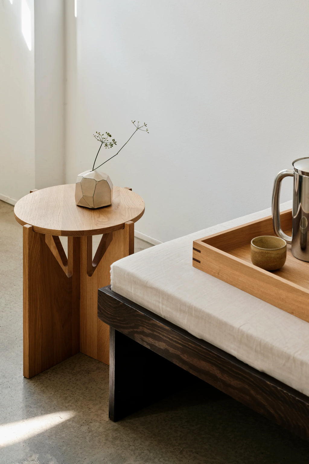 Kristina Dam Simple Stool, a modern minimalist solid oak stool featuring a round top and a striking geometric base with triangular cutouts, showcasing the natural light oak wood grain. This versatile Scandinavian design piece functions perfectly as a bedside table or a contemporary accent table for living rooms and japandi spaces.