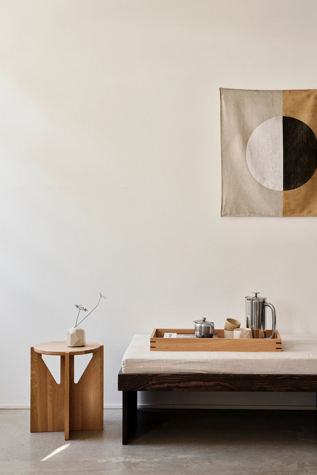 Kristina Dam Simple Stool, a minimalist solid oak wood stool featuring a round top and a distinctive geometric base with three interlocking flat legs and carved cutouts, showcasing beautiful natural light oak grain. This contemporary Scandinavian design makes it a versatile accent piece, perfect for living rooms, as a chic bedside table, or a unique plant stand in modern interiors.