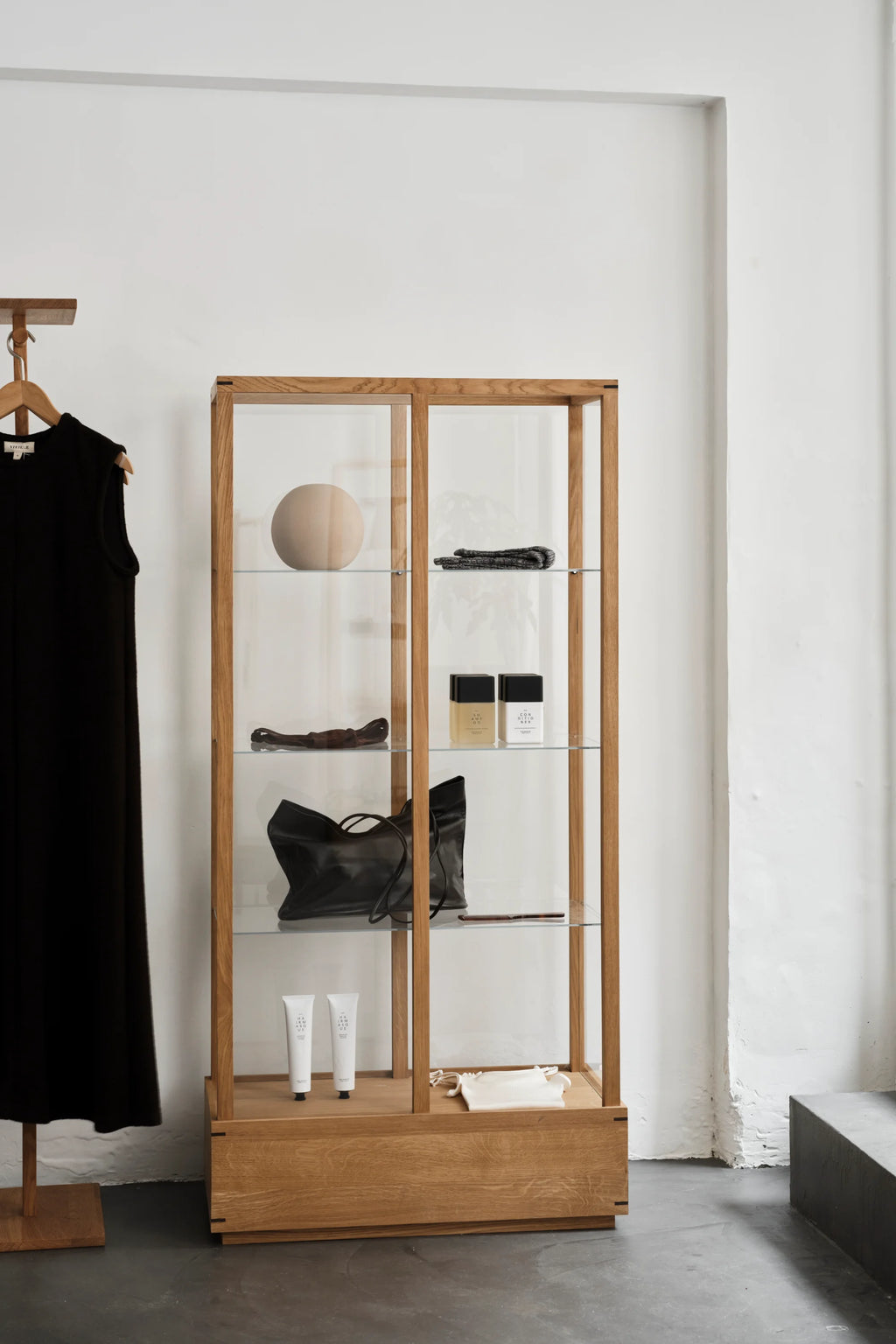 Kristina Dam Japanese Cabinet L, a modern minimalist display cabinet crafted from natural solid oak with clear glass panels and interior shelves, featuring a clean, rectangular silhouette and a sturdy wooden base. This Scandinavian-inspired storage cabinet is perfect for showcasing decor in living rooms or as a stylish retail display for contemporary interiors.