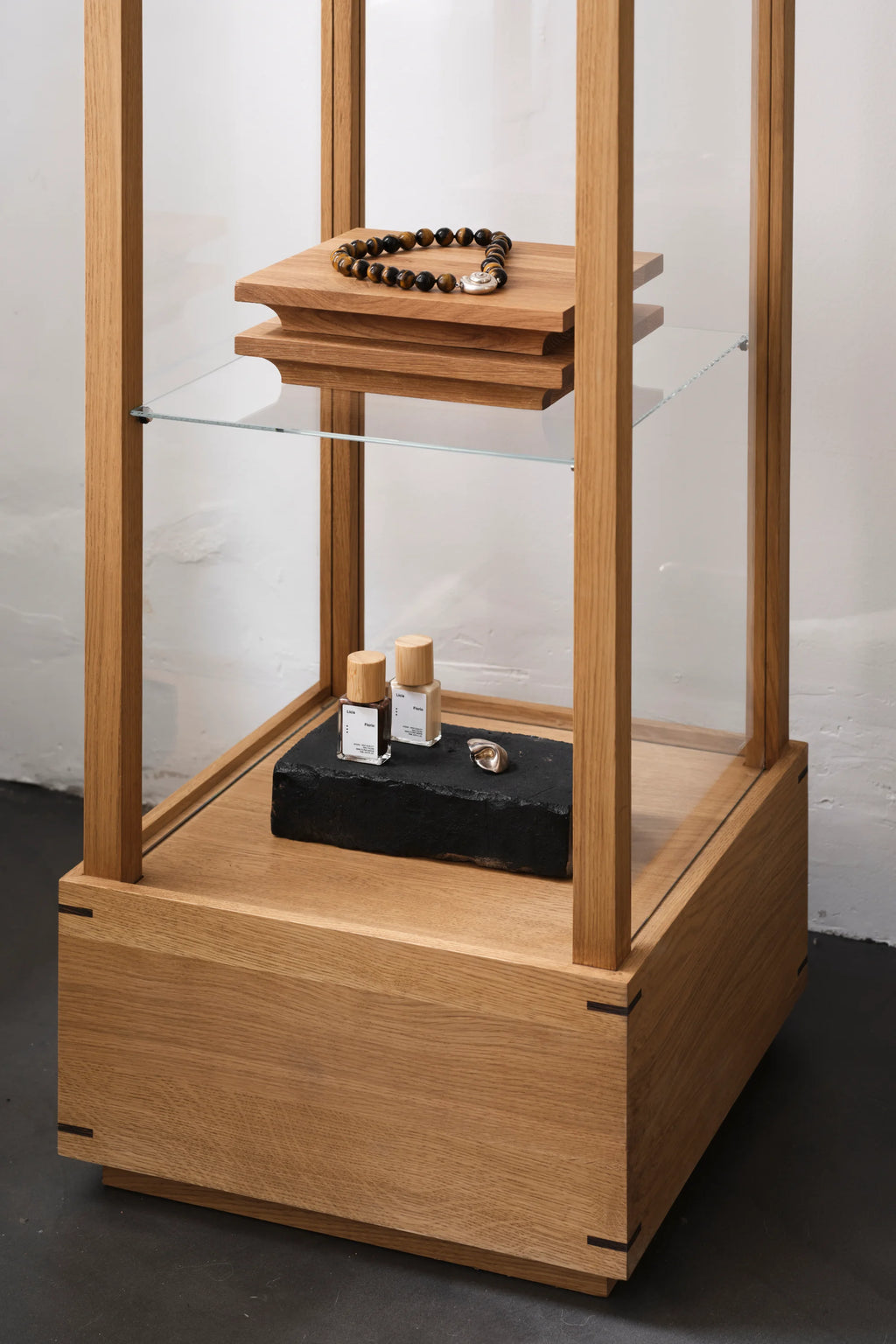 Kristina Dam Capital Podium, a modern minimalist display stand crafted from natural solid oak with a clean-lined architectural design, featuring clear glass shelves and a lower storage cabinet with exposed dovetail joints.