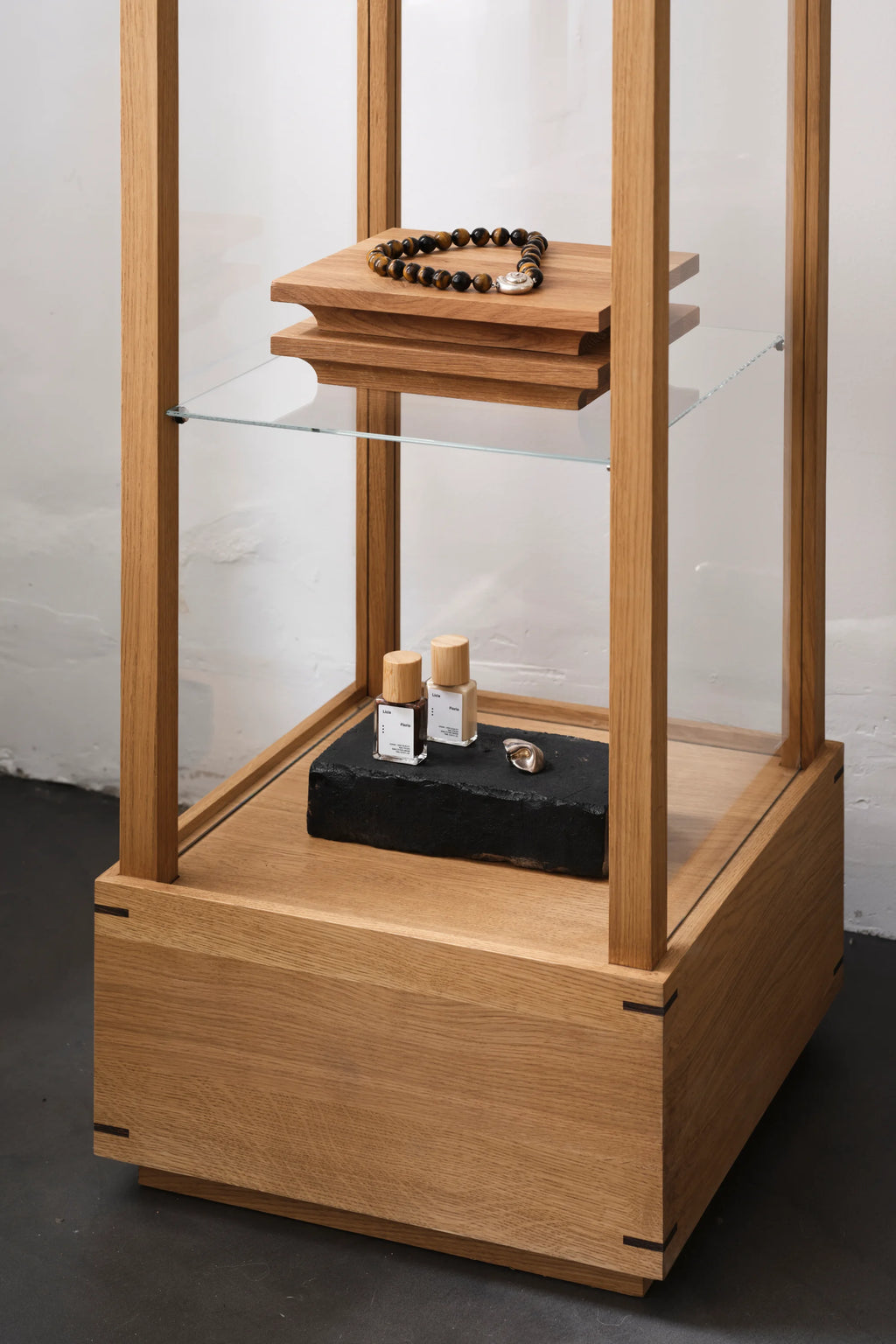Kristina Dam Japanese Cabinet M, a minimalist display cabinet crafted from natural solid oak with clean lines and subtle black joinery details. This contemporary showcase features clear glass panels and an internal glass shelf, providing elegant storage for collectibles or retail merchandise. Perfect as a Scandinavian or Japanese-inspired accent in living rooms, dining areas, or modern retail spaces.