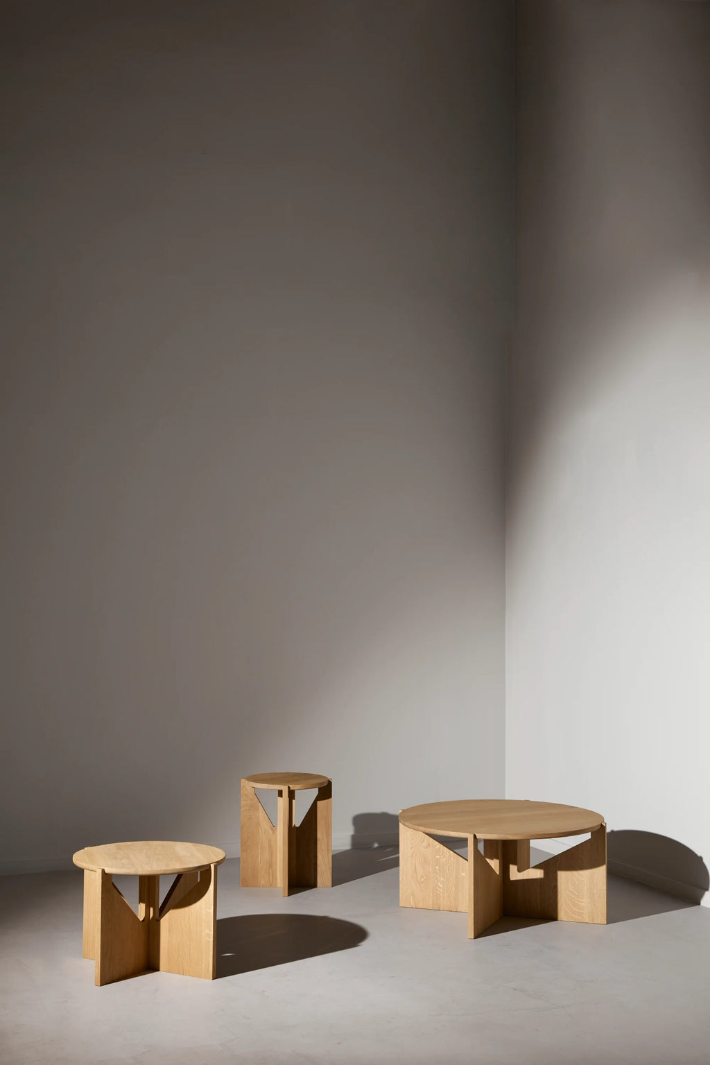 Kristina Dam Simple XL Coffee Table, a modern minimalist round coffee table crafted from beautiful light natural solid oak wood with visible grain and a smooth finish. Its distinctive sculptural base features intersecting flat panels that create a geometric silhouette, offering an architectural touch. This contemporary solid oak coffee table is perfect as a living room centerpiece for Scandinavian, organic modern, or minimalist interiors.