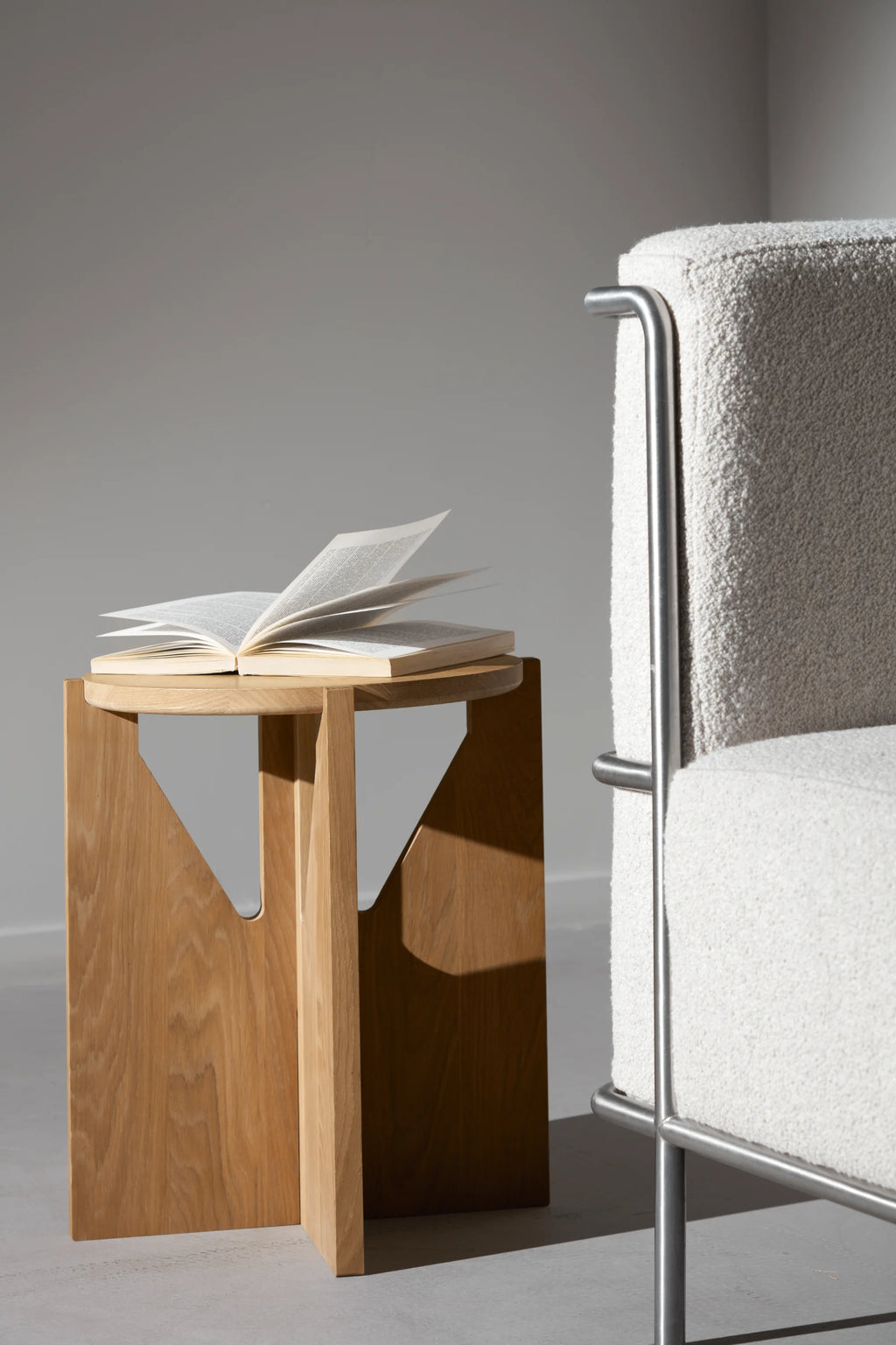 Kristina Dam Simple Stool, a modern minimalist solid oak stool featuring a smoothly rounded top and a sculptural base of three intersecting flat oak panels, forming striking geometric cut-outs. Crafted from natural light oak with a clean, contemporary design, this versatile piece functions as a stylish accent table or small side table.