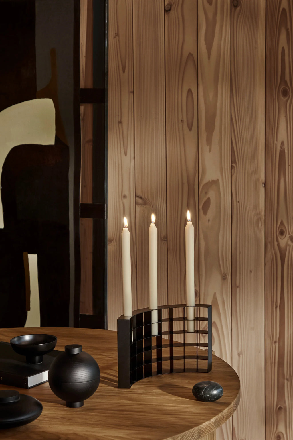 Kristina Dam Mesh Candle Holder, a modern minimalist candelabra crafted from matte black powder-coated steel, featuring a distinctive graphic grid design and a curved silhouette that elegantly holds three tapered candles.