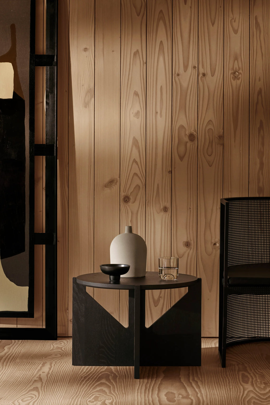 Kristina Dam Simple Coffee Table, a striking matte black solid oak coffee table featuring a smooth round top and a bold, sculptural geometric base with triangular cutouts. Its minimalist design showcases clean lines and a subtle wood grain texture, embodying a modern brutalist aesthetic.