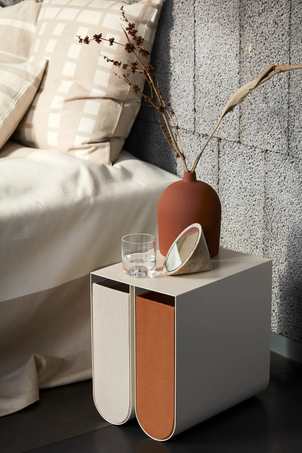 Kristina Dam Curved Side Table, a sleek Scandinavian bedside table featuring a light greige powder-coated steel frame with a clean rectangular top and elegant curved corners. Its unique front showcases two half-cylinder storage compartments, upholstered in contrasting cream and burnt orange fabric.