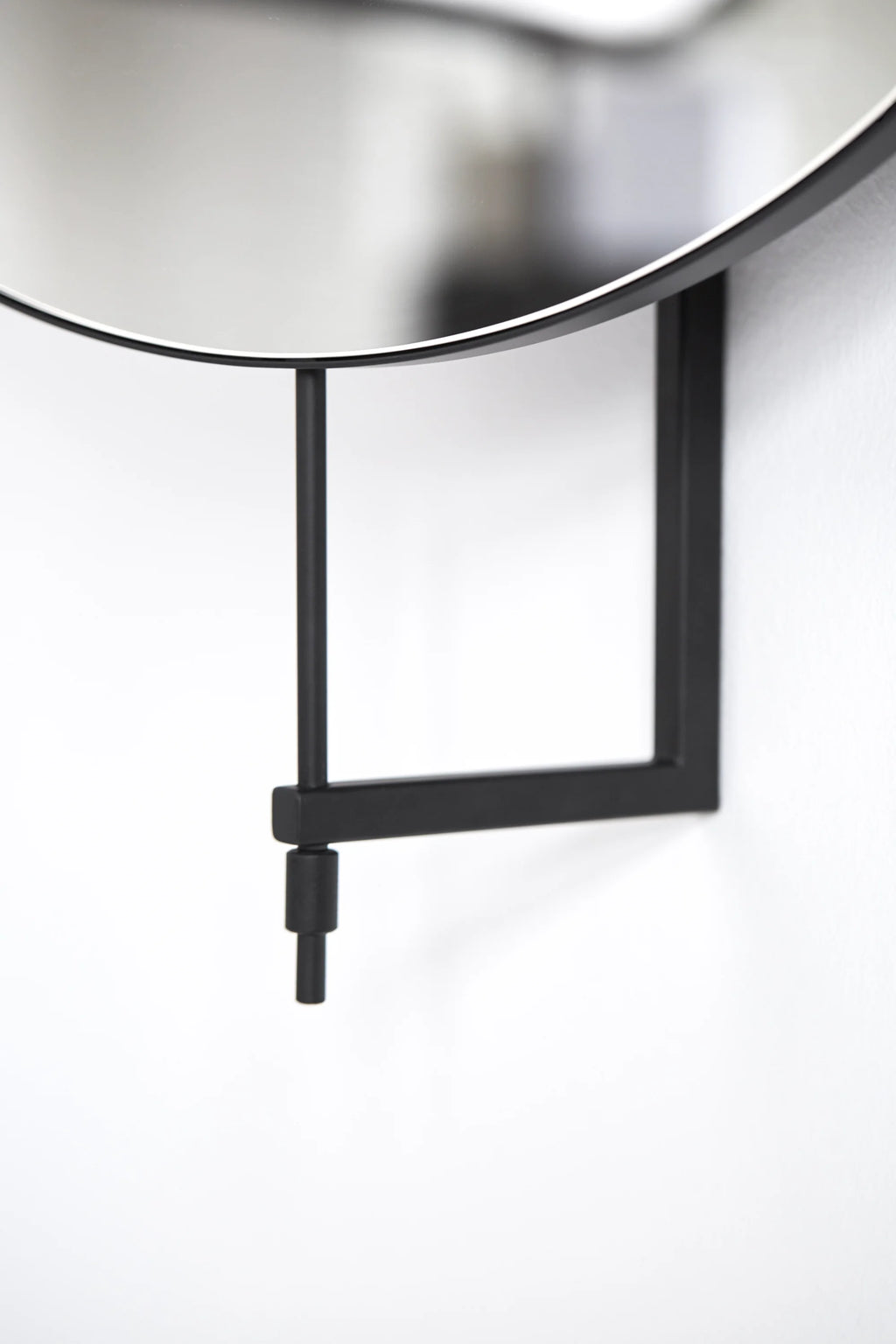 Kristina Dam Rotating Mirror, a sleek round wall mirror featuring a matte black metal frame and an innovative geometric matte black steel wall bracket that allows for easy rotation. Its clean lines and modern minimalist design make it a perfect accent mirror for Scandinavian living rooms, contemporary entryways, or stylish bathrooms.