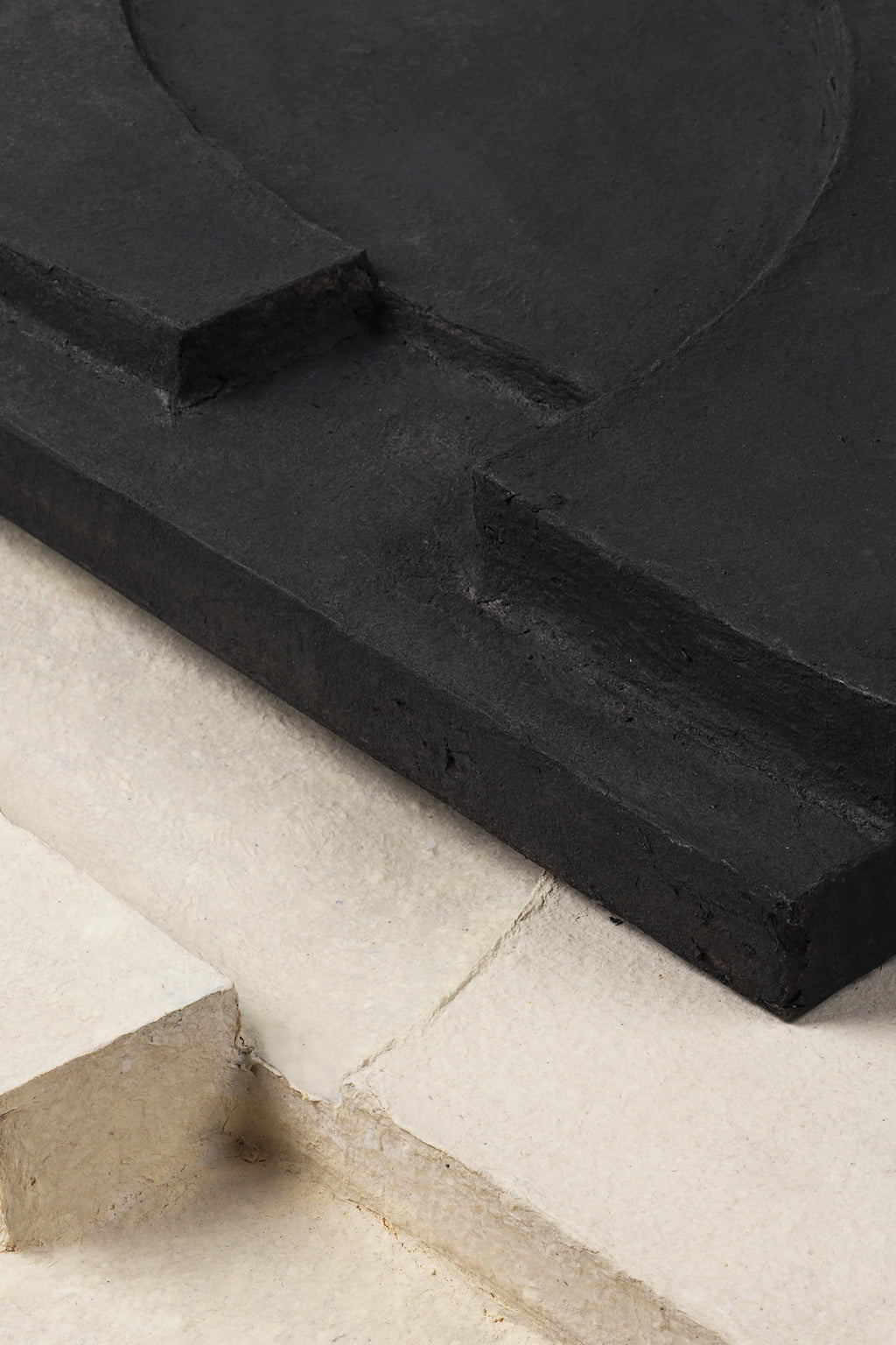 Kristina Dam Serif Relief M, a striking brutalist-inspired wall art piece featuring a raised matte black fiber concrete sculptural relief with a raw, textured finish, contrasted by an off-white background. This contemporary geometric art showcases abstract architectural forms and organic modern lines, offering depth and visual intrigue. Ideal for minimalist living rooms, gallery walls, or home offices seeking a bold, textured statement.
