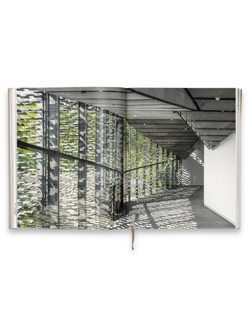 Book Kuma. Complete Works 1988–Today, open to a high-quality glossy page showcasing a modern architectural interior with a glass facade and intricate sunlight patterns on the concrete floor. This elegant architecture book is perfect for design enthusiasts and students of contemporary building.