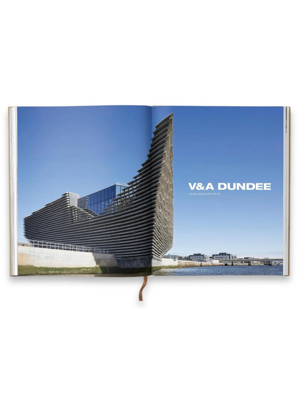 Book Kuma. Complete Works 1988–Today, open architectural book displaying a vibrant blue sky and a striking modern building, the V&A Dundee, with layered concrete panels and glass sections by a waterfront. This premium architecture book is perfect for design enthusiasts, students, and professionals interested in contemporary architectural design and history.