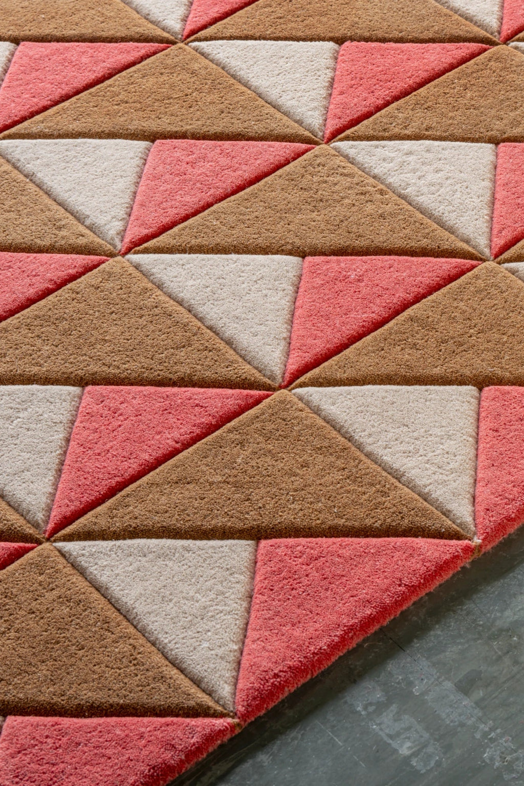 Layered Triangle Wool Rug, a premium textured rug featuring a geometric pattern of coral pink, light beige, and brown triangular wool patches. Perfect for adding a modern, cozy accent to living roo...