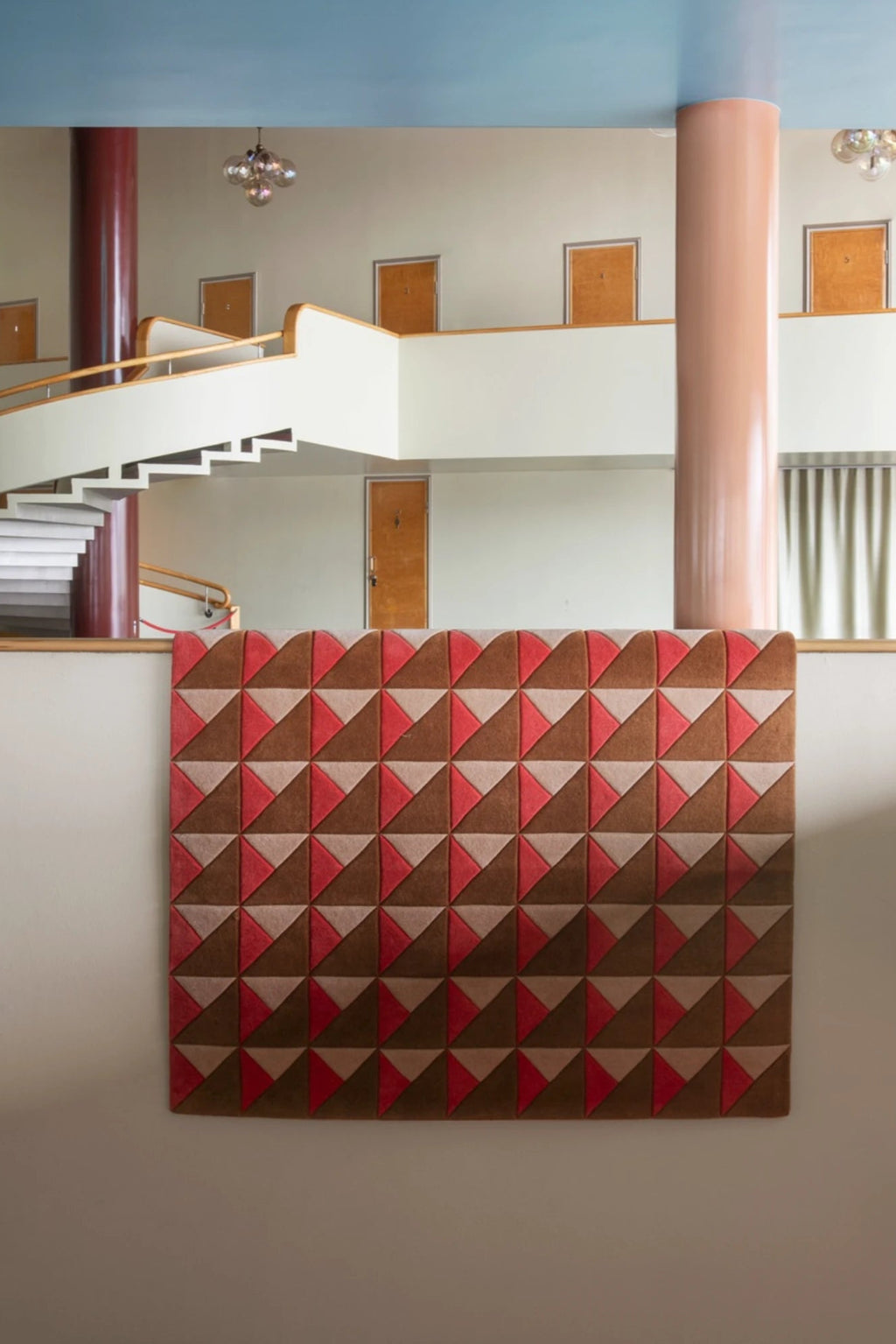 Layered Triangle Wool Rug, a modern geometric area rug with a repeating pattern of red, brown, and beige triangles. Perfect for adding a bold design statement to contemporary interiors.