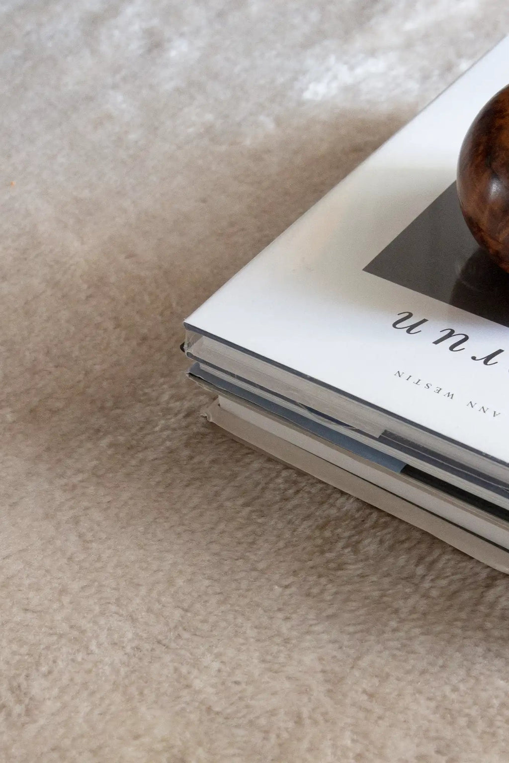 Layered Artisan Wool Rug, a soft, plush beige or light brown wool area rug with a subtle textured pile, visible beneath a stack of books. Perfect for adding warmth and comfort to any living room or...