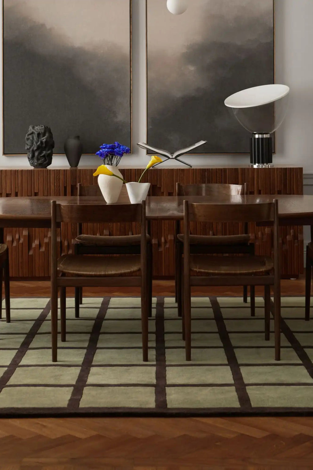 Layered Avenue Checked Wool Rug, a modern green and brown checked area rug with a geometric pattern, grounding a dining room setting with a wooden table and chairs. Perfect for adding contemporary...