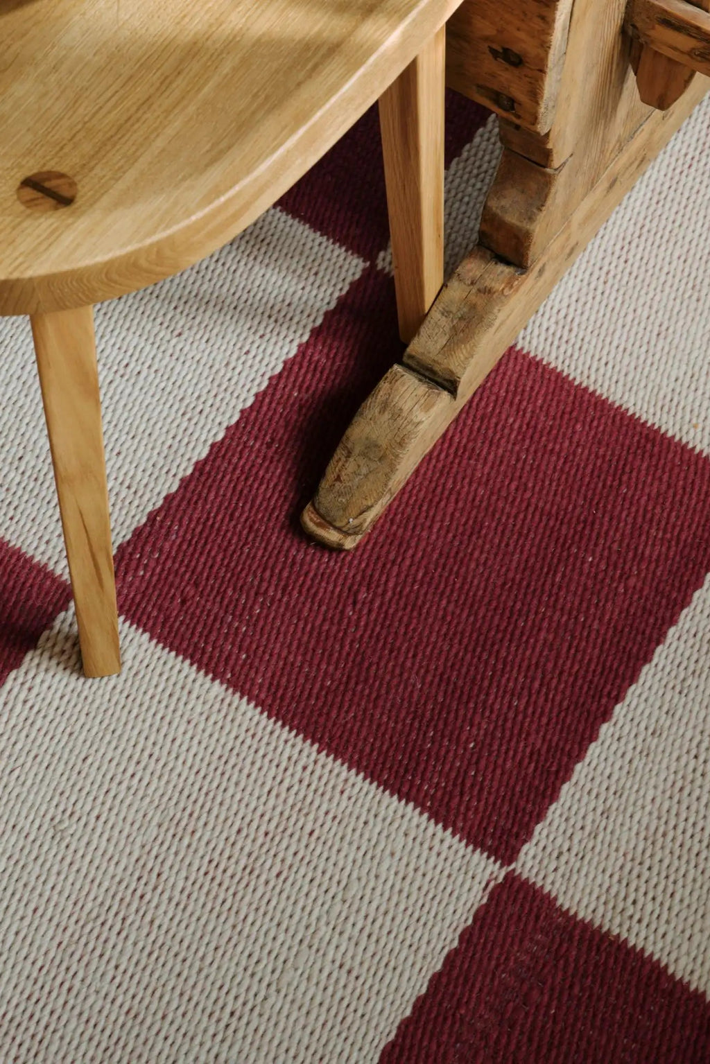 Layered Chess Wool Rug, featuring a bold geometric pattern of large maroon and off-white squares, crafted from natural wool fibers. Perfect for adding a cozy, Scandinavian-inspired accent to any li...