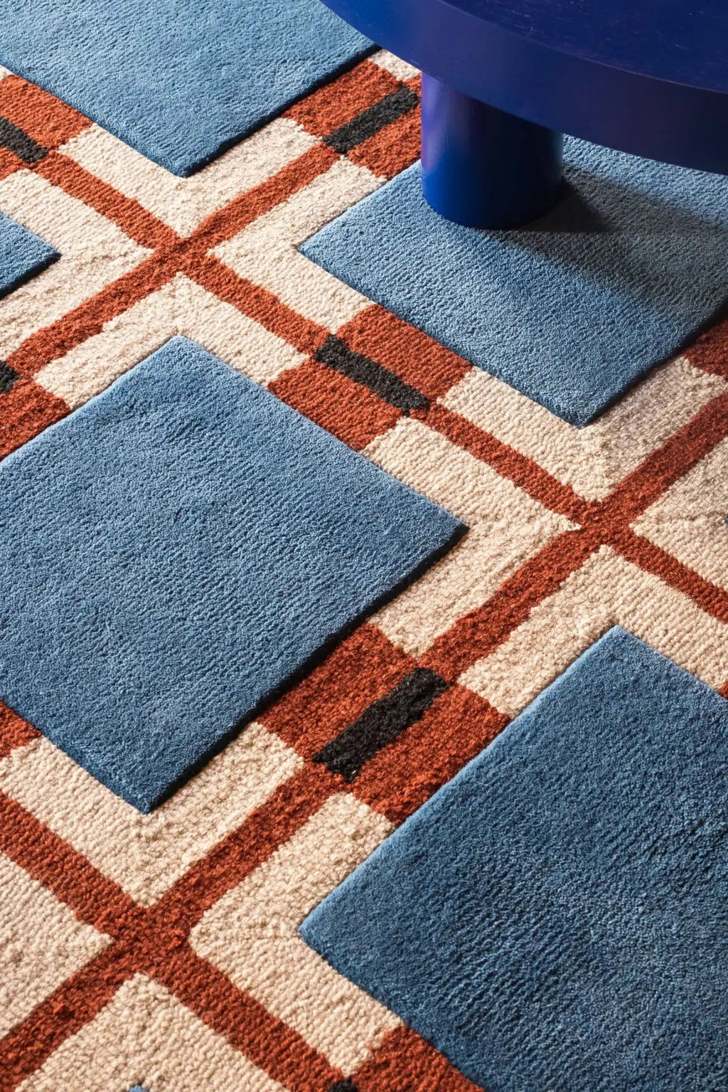 Layered Berry Rain Wool Rug, a thick, hand-tufted wool rug featuring a geometric pattern of terracotta, cream, blue, and black. Perfect for adding warmth and modern style to any living room or bedr...