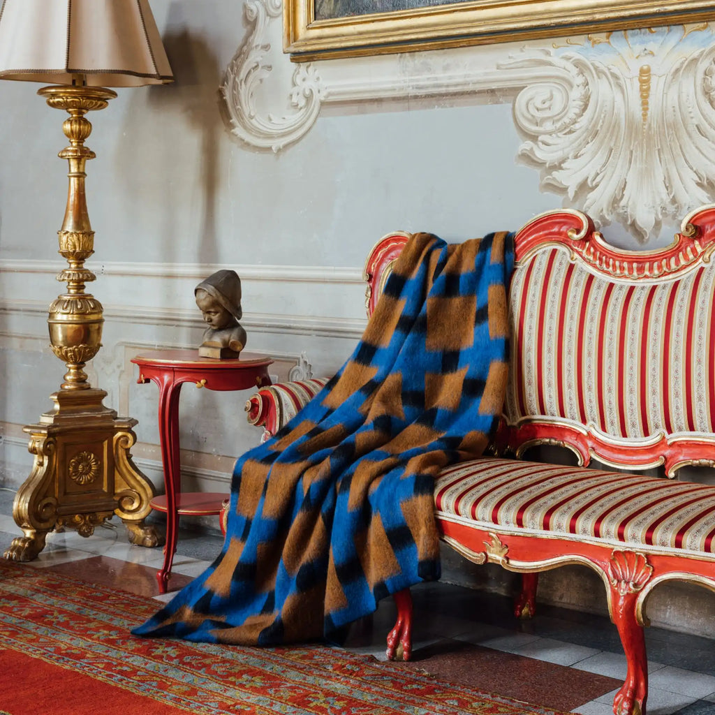Layered Fall Foliage Oversized Blanket, a plush mohair throw with a striking brown, black, and blue geometric pattern draped over a red baroque sofa. Perfect for adding a luxurious, warm accent to...
