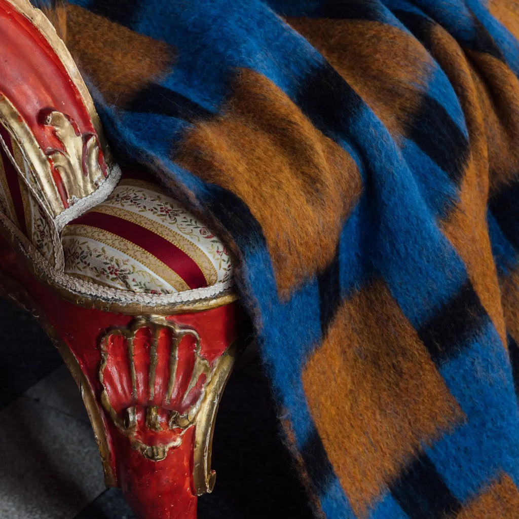 Layered Fall Foliage Oversized Blanket, a cozy blue, black, and amber block-patterned mohair throw with a soft, shaggy texture draped over a vintage red and gold chair. Perfect for adding warmth an...