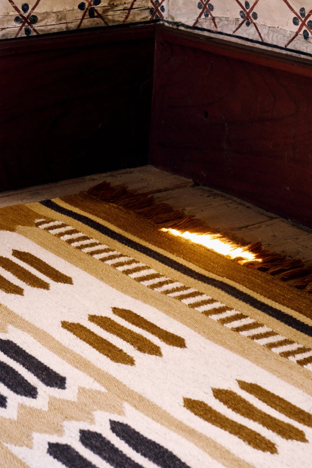 Layered Hilma Wool Rug, a rustic hand-woven area rug featuring a striped geometric pattern in natural tones of cream, tan, and dark brown with fringe edges. Perfect for adding warmth and texture to...