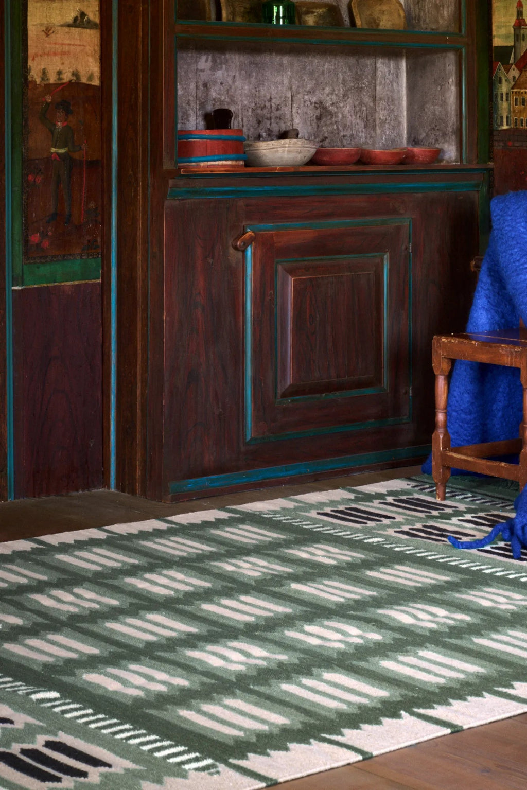 Layered Hilma Wool Rug, a hand-tufted green and white wool area rug with a bold, modern ikat pattern and black accents. Perfect for adding contemporary style and warmth to living rooms and bedrooms.