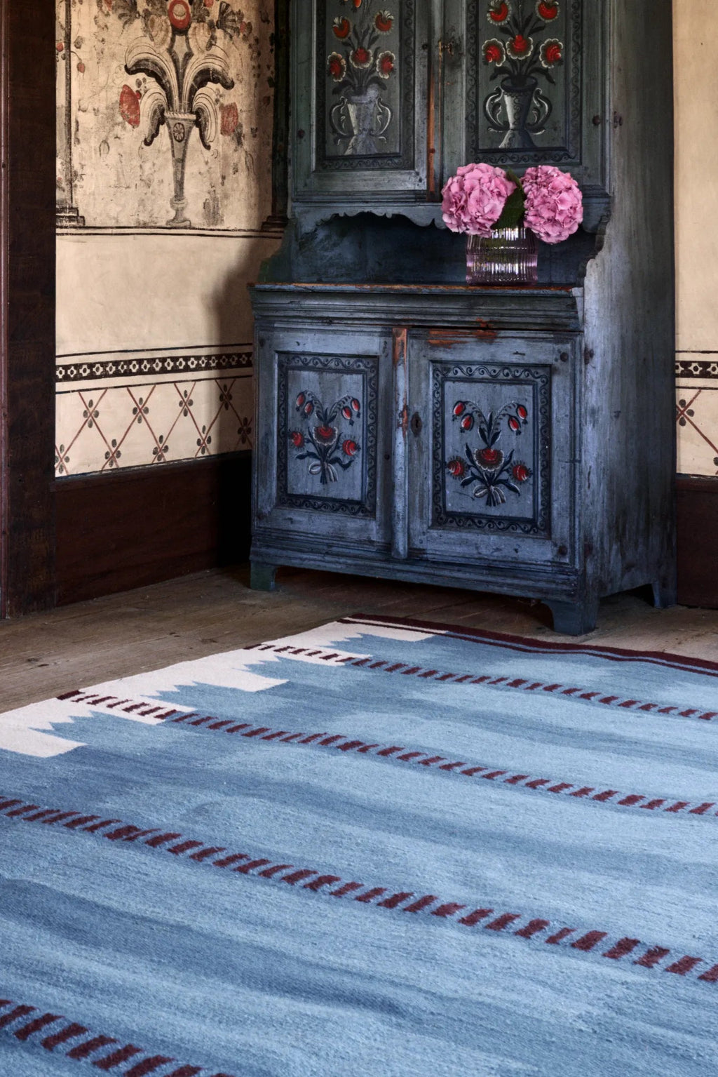 Layered Iris Wool Rug, a light blue handwoven wool area rug with subtle white and burgundy striped patterns, featuring a soft, textured pile. Perfect for adding warmth and style to a living room or...