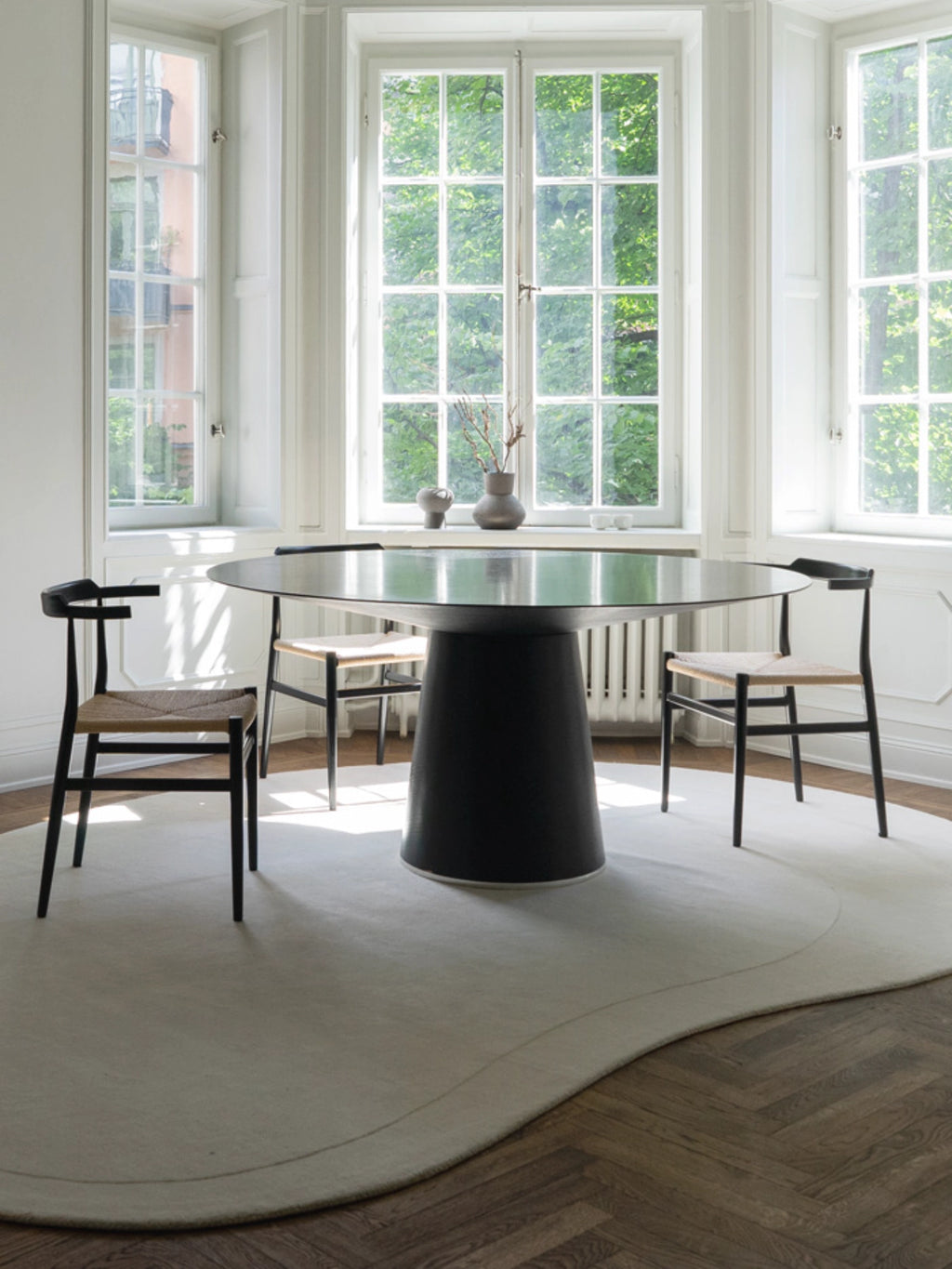 Layered Residue Wool Rug, a soft cream-colored wool area rug featuring a unique organic, irregular shape with gently curving edges, creating a fluid silhouette on the dark parquet flooring.