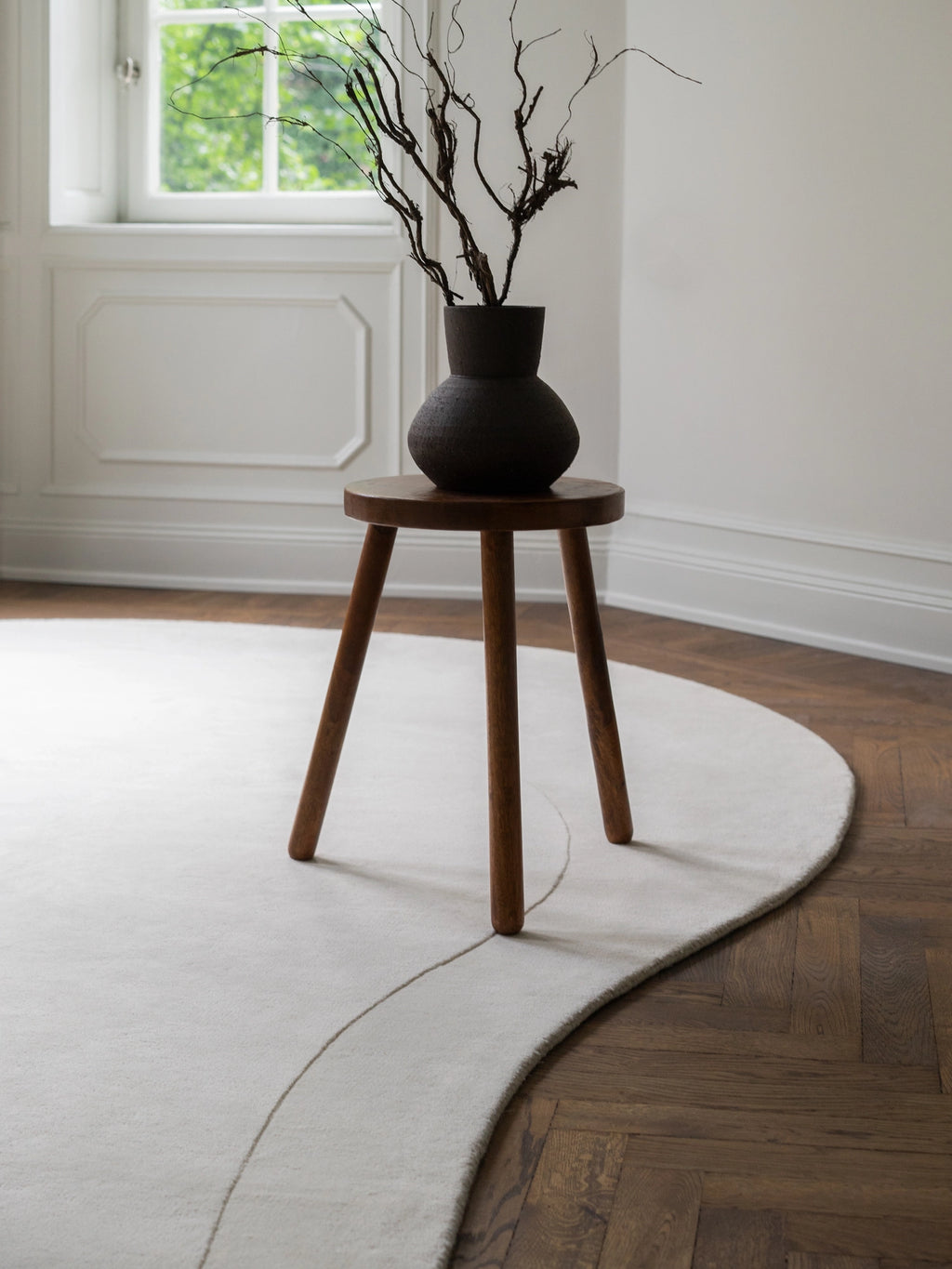Layered Residue Wool Rug, a plush hand-tufted wool area rug in a serene off-white cream color, featuring a unique organic curved shape and a subtle lighter line detail across its surface.