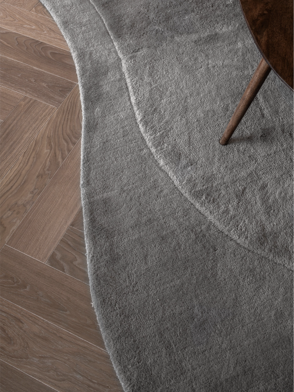 Layered Residue Wool Rug, a soft grey premium wool area rug with a plush, textured pile and an organic, irregular shape featuring subtle wavy contours that create a layered effect.
