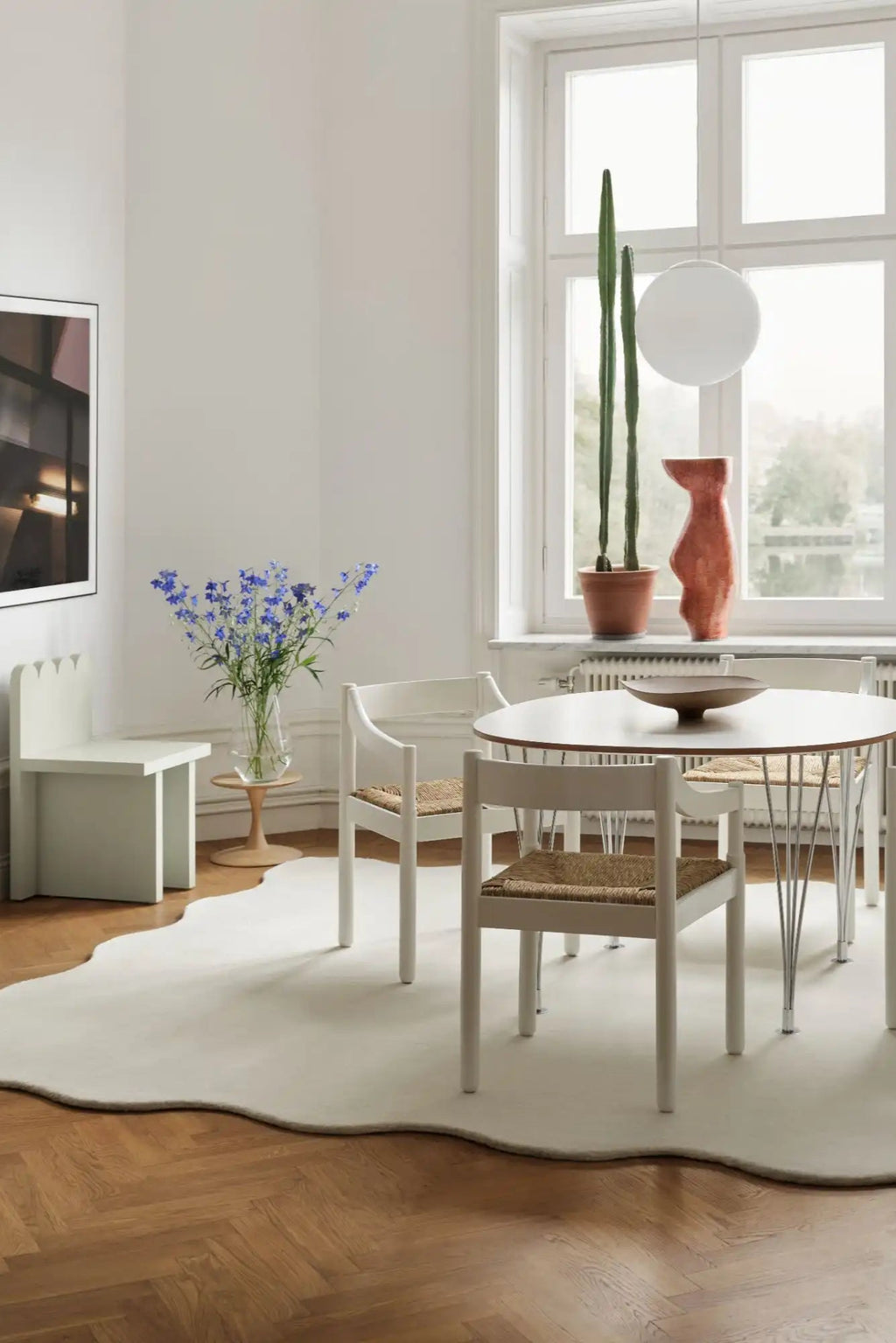 Layered Scallop Wool Rug, a large creamy white area rug with a unique wavy, irregular edge design on a herringbone wood floor. Perfect for adding a soft, organic modern touch to living rooms or din...