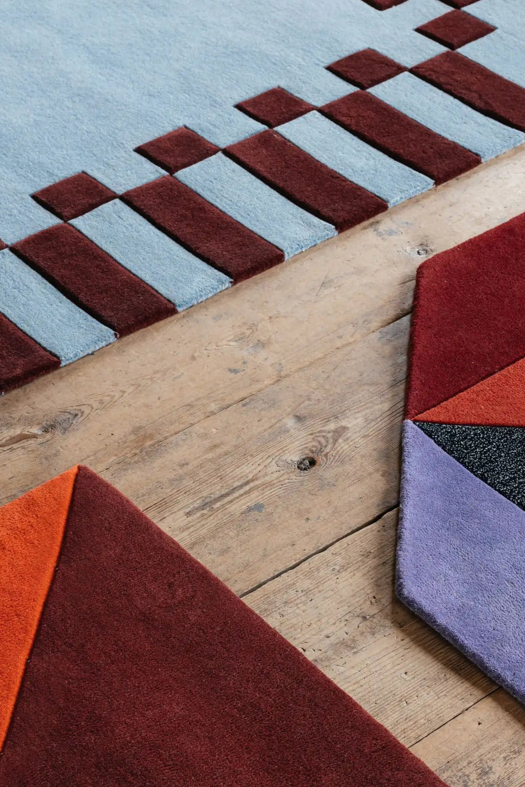 Layered Frame Wool Rug, showcasing a light blue and maroon geometric pattern alongside colorful abstract segments in red, orange, and purple. This modern wool rug adds a unique design element to an...