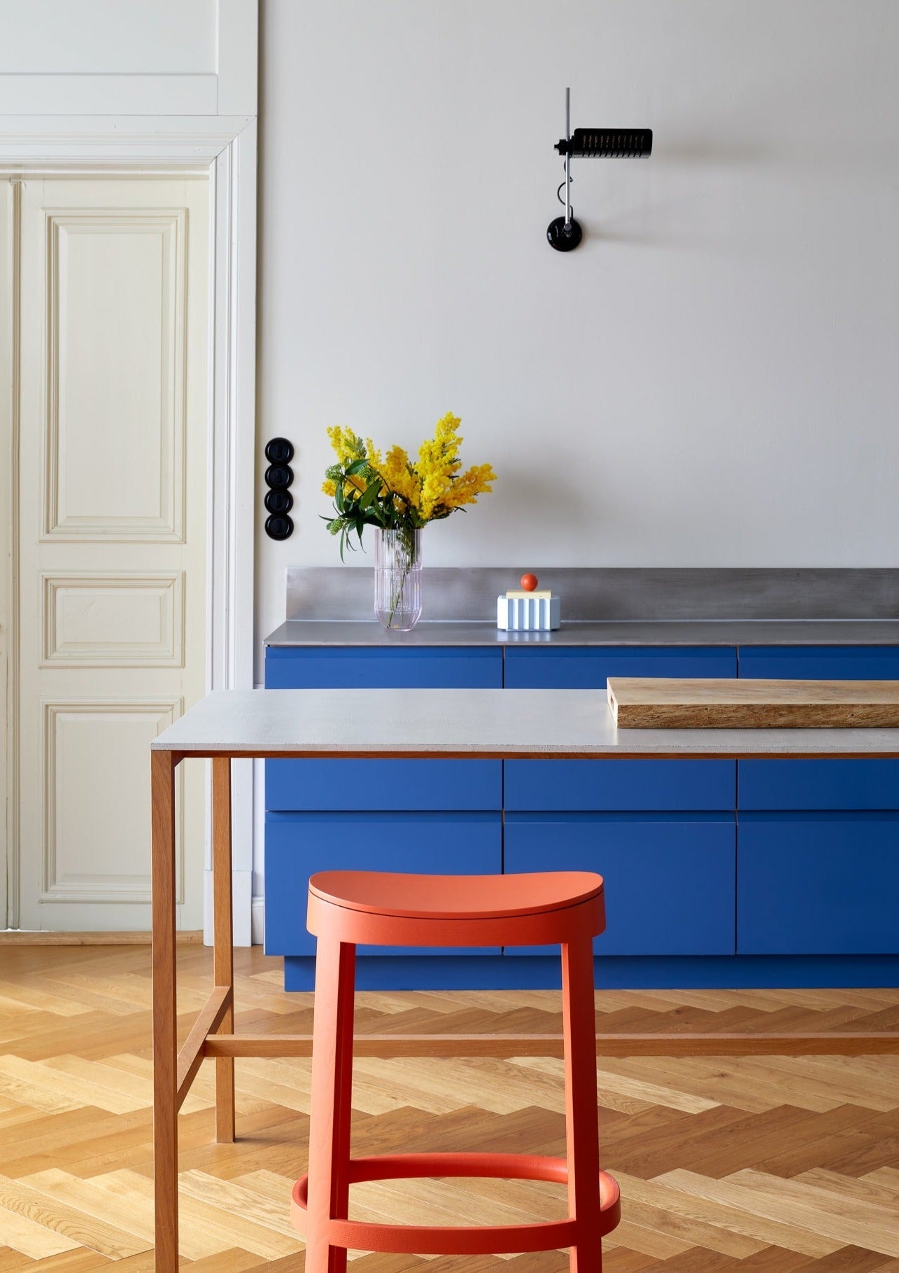 Modern kitchen with blue cabinets, a red lammi bar stool, and yellow flowers.