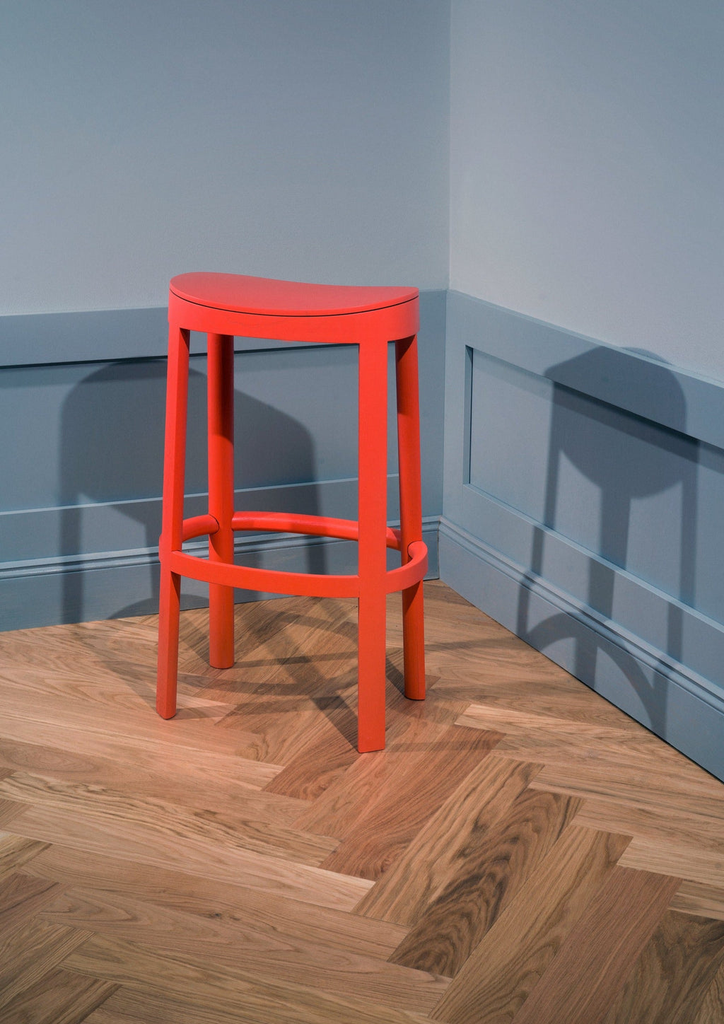 Made by Choice Lammi Bar Stool, a striking coral red painted solid wood bar stool featuring a smooth matte finish and an ergonomically curved saddle seat. Its modern minimalist design showcases clean, sturdy legs and a circular footrest, embodying Scandinavian style. Perfect as a vibrant kitchen island stool or contemporary bar seating in modern homes.