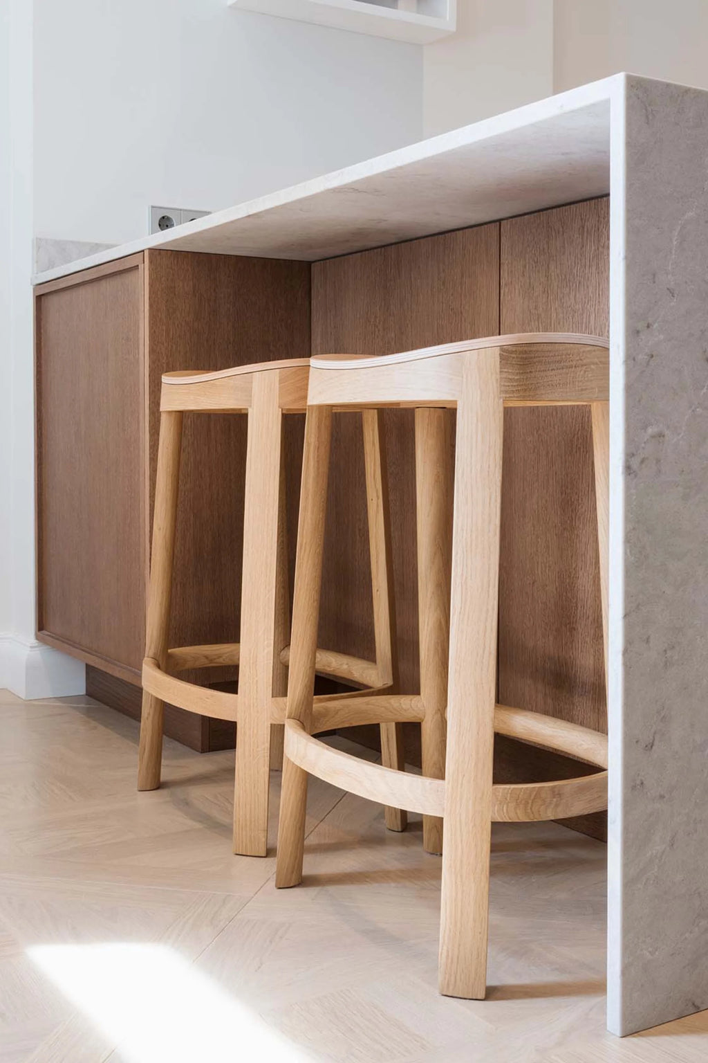 Made by Choice Lammi Bar Stool, a minimalist Scandinavian solid oak bar stool with a gently curved seat and sturdy square legs, crafted from light natural wood. This modern wooden counter stool features an integrated footrest for comfort and clean, organic lines. Perfect for contemporary kitchen islands or stylish bar seating in modern minimalist homes.