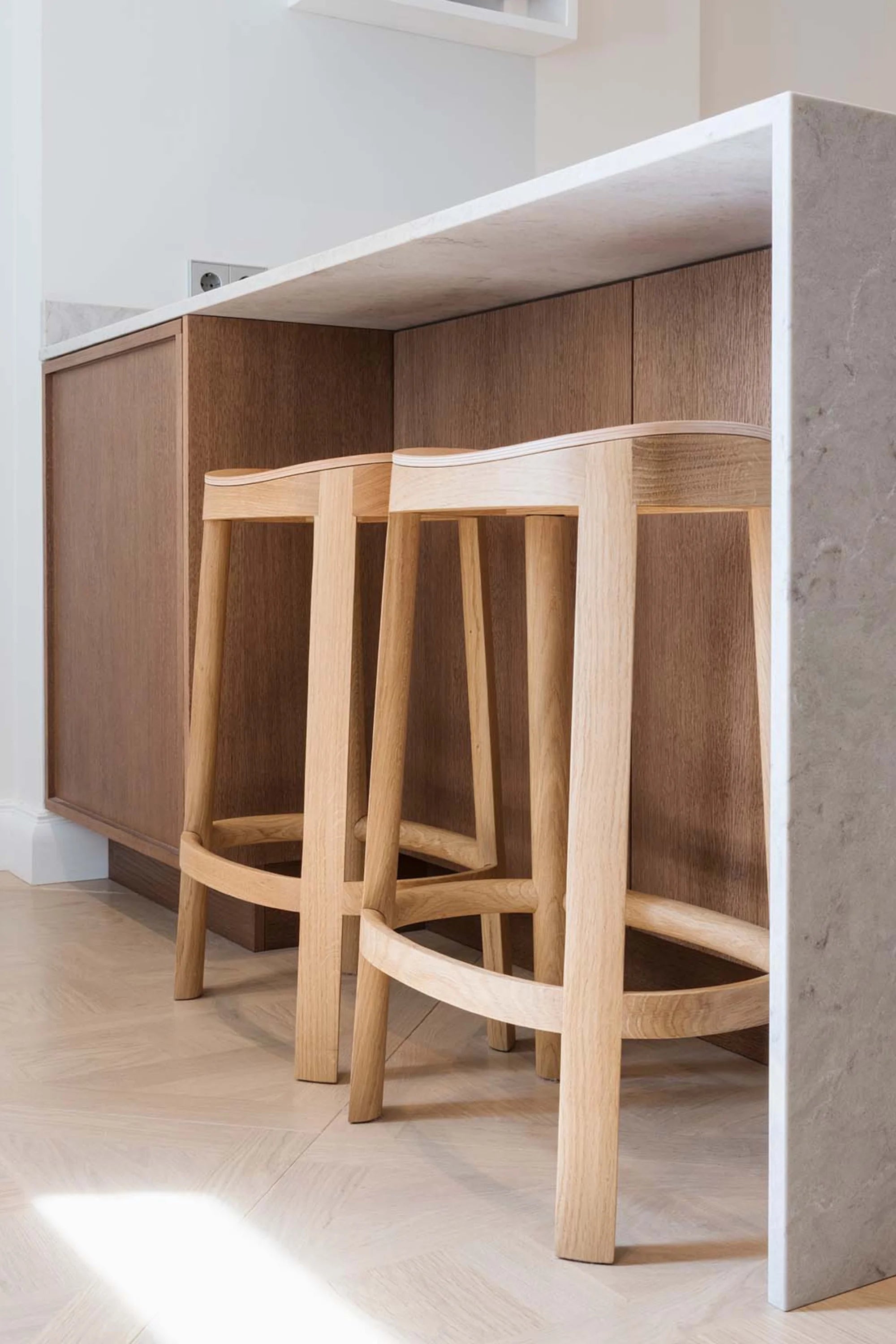 Wooden bar stools in front of a kitchen counter with wooden cabinets.