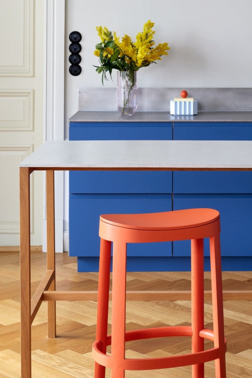 Modern kitchen with blue cabinets, a red stool, and a wooden table.