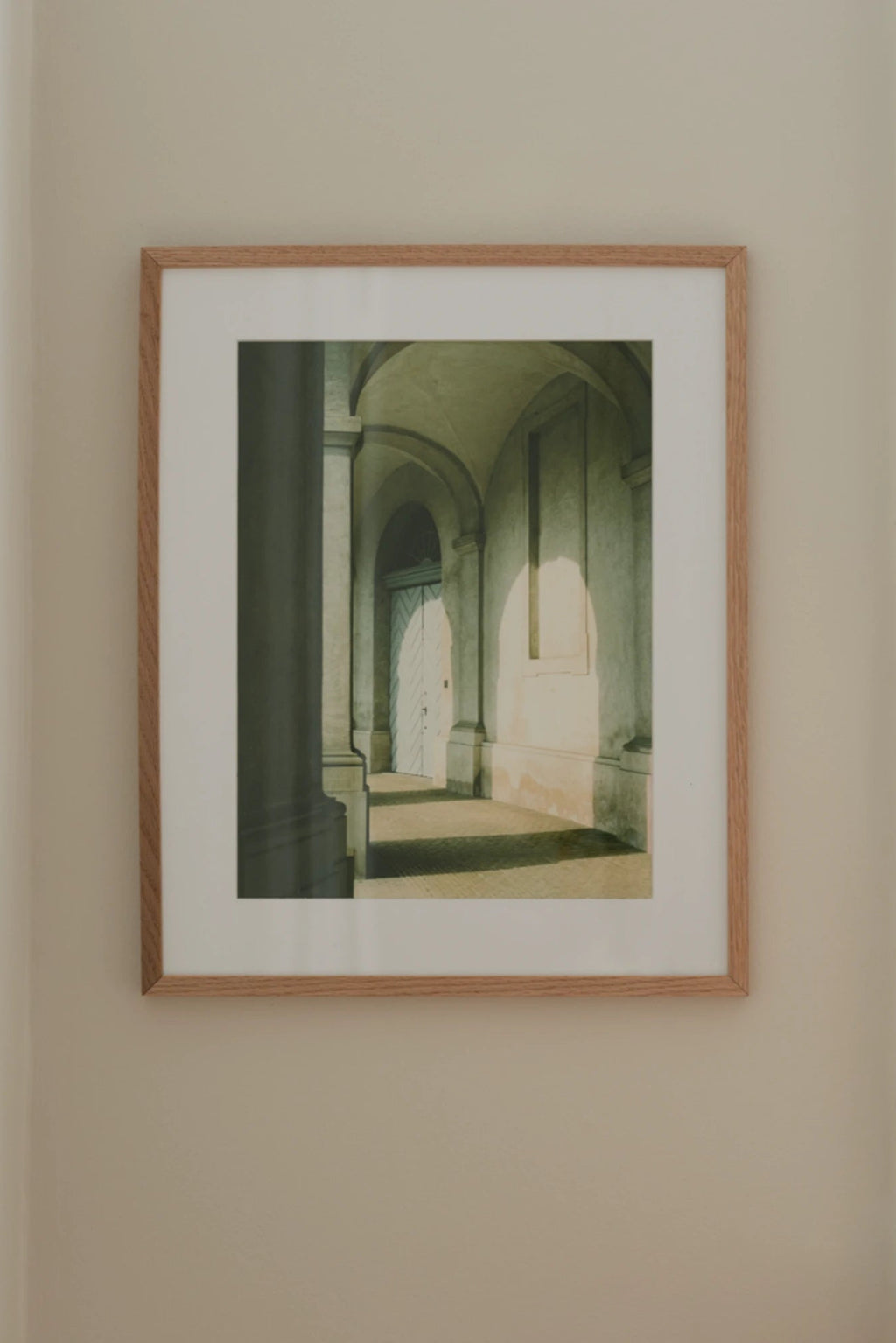 The Poster Club Morning Sun, an atmospheric architectural photography print capturing a sunlit arched hallway with a distinct light blue door, rendered in muted greens, greys, and warm cream tones.