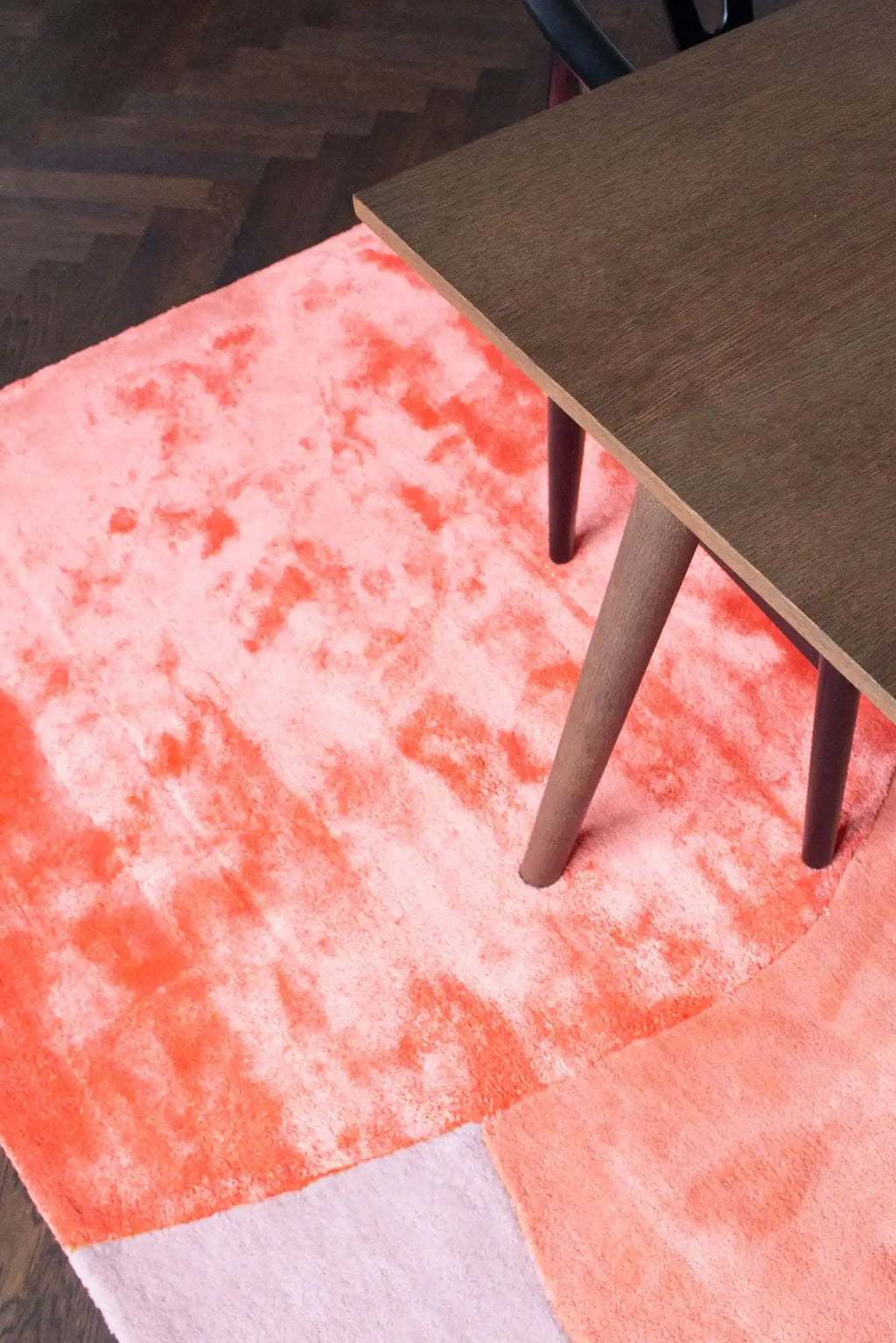 Layered Flower Field Wool Rug, a vibrant pink and coral area rug with a soft, textured pile and abstract color block design, partially visible under a modern wooden table. Perfect for adding a pop...