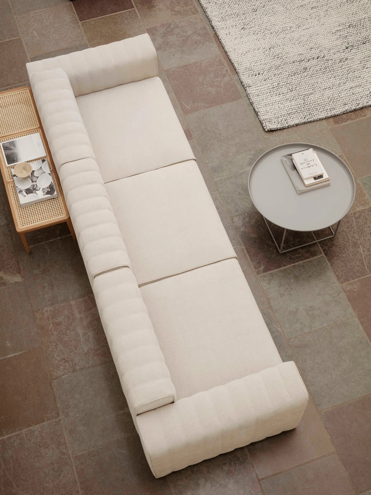 NORR11 Le Roi Bench, a long, minimalist cream fabric bench with ribbed backrest against a natural cane side table. A luxury modern furniture piece for elegant living spaces.