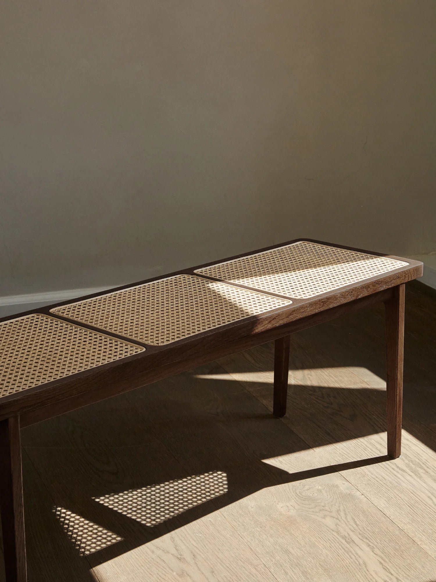 NORR11 Le Roi Bench, a premium dark brown oak wooden bench with three natural cane weaving panels, creating elegant sun patterns on light hardwood floor. Perfect for sophisticated entryway or living room styling.