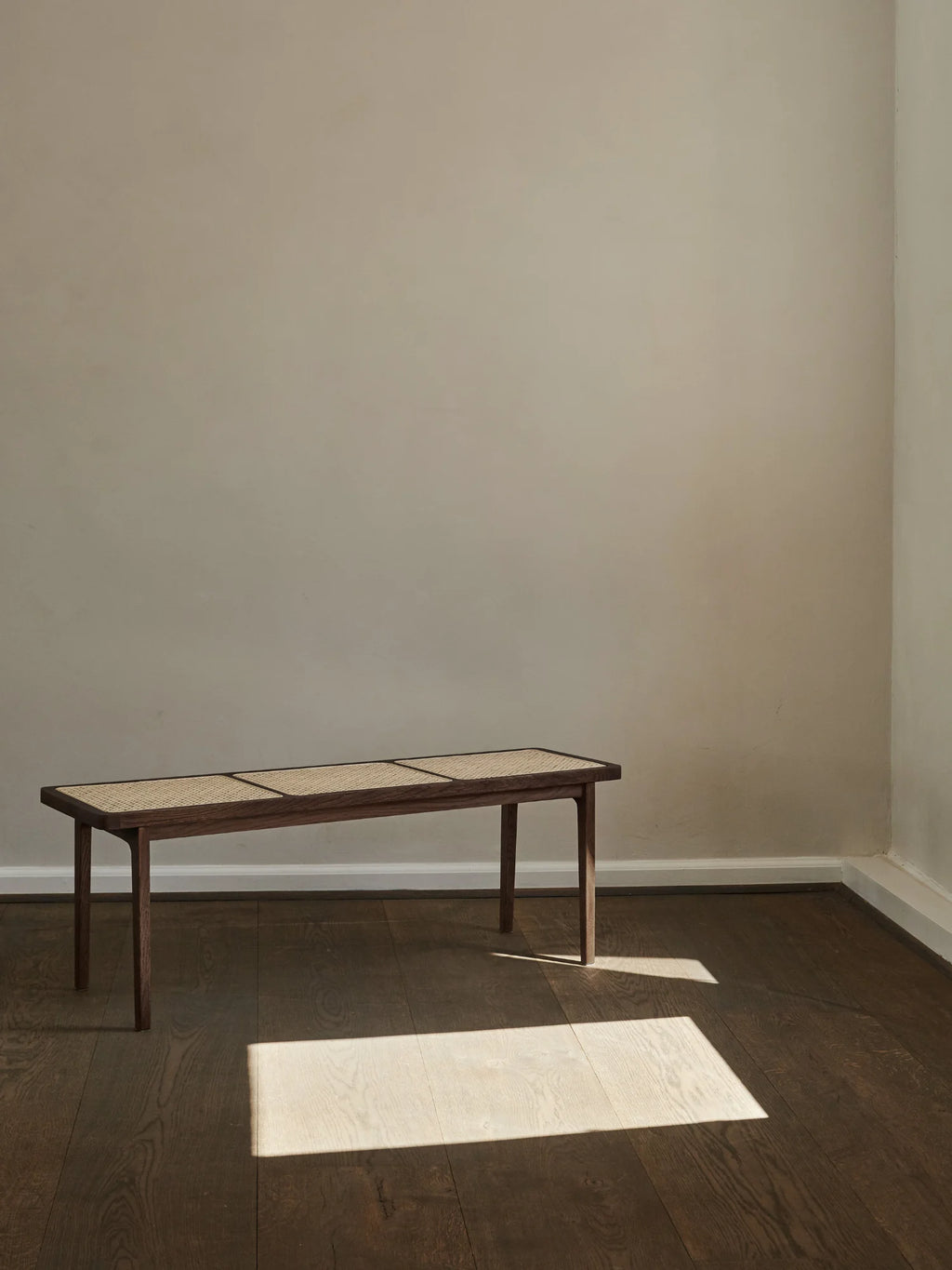 NORR11 Le Roi Bench, a premium dark brown solid wooden bench with three woven natural cane panels, pictured in a minimalist room with natural light. Perfect for entryways or living spaces.