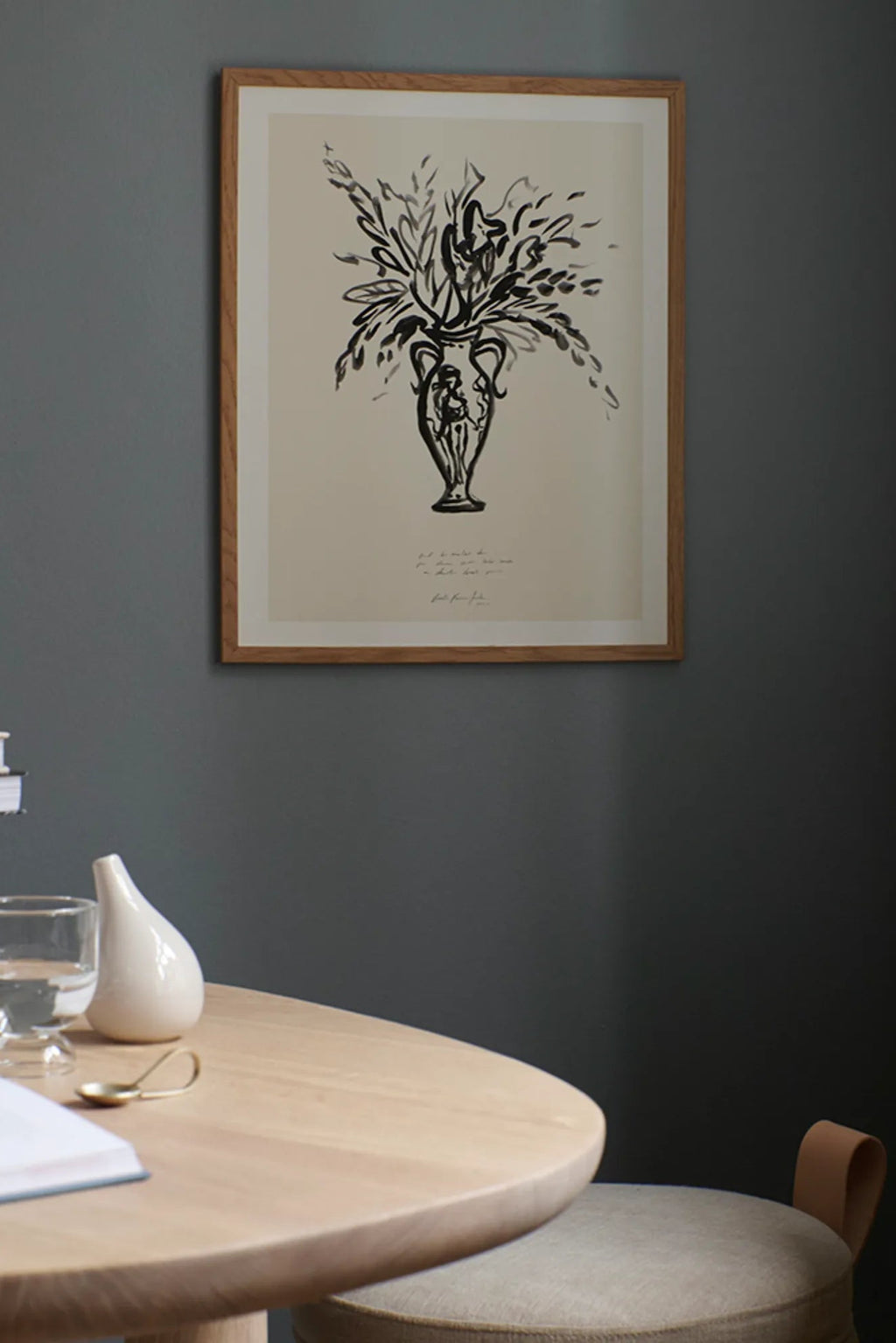 The Poster Club Condolences 02, a striking abstract art print featuring an expressive black sketch illustration of a classical urn-shaped vase overflowing with organic foliage, set against a warm off-white paper background. This minimalist wall art is elegantly framed in a light natural oak frame with a crisp white mat, enhancing its contemporary appeal.