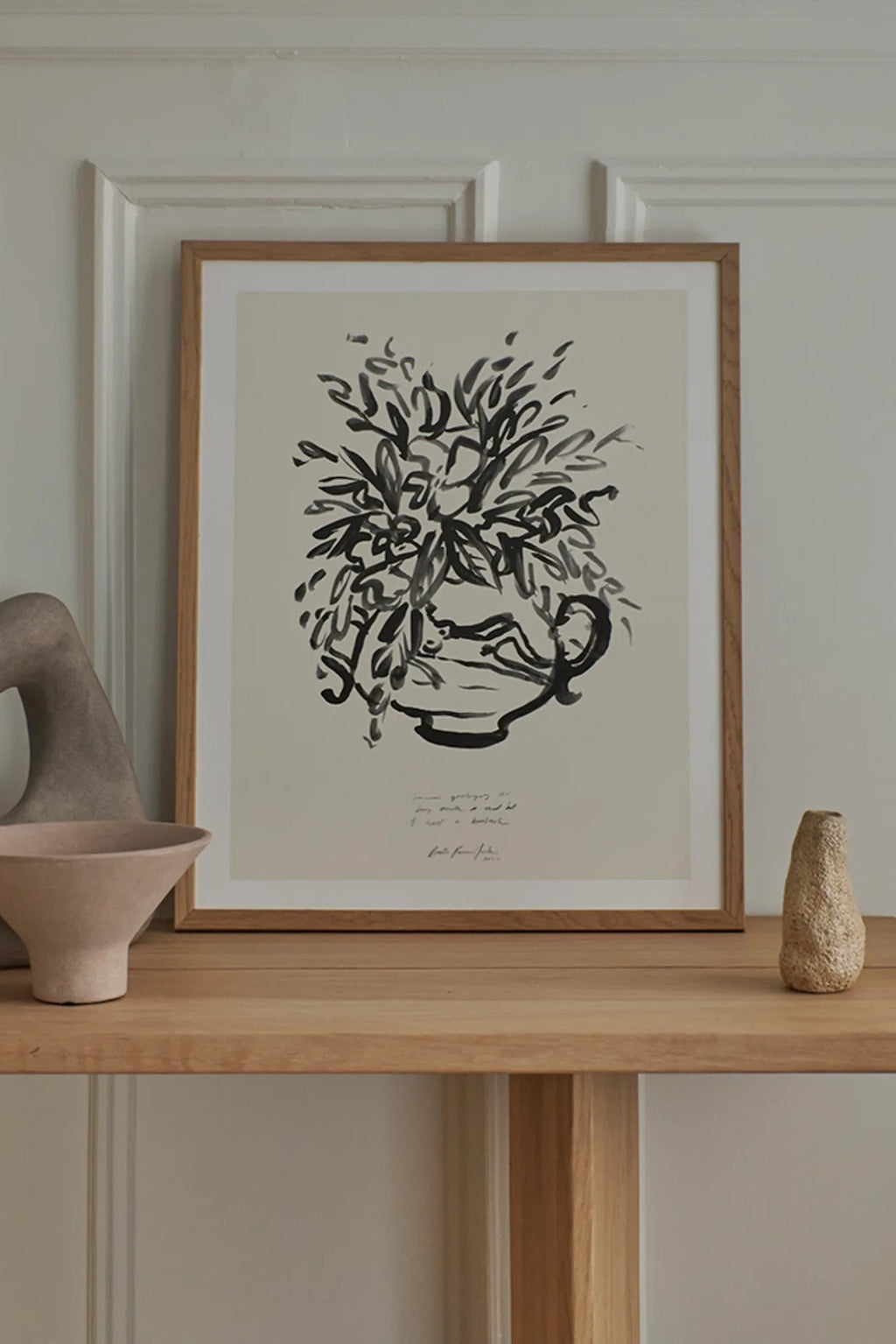 The Poster Club Condolences 04, an expressive abstract art print featuring bold black brushstrokes forming a stylized vase with organic foliage on an off-white paper background, presented in a natural oak frame with a clean white mat. This modern minimalist wall art is ideal for Scandinavian living rooms, Japandi bedrooms, or contemporary gallery walls.