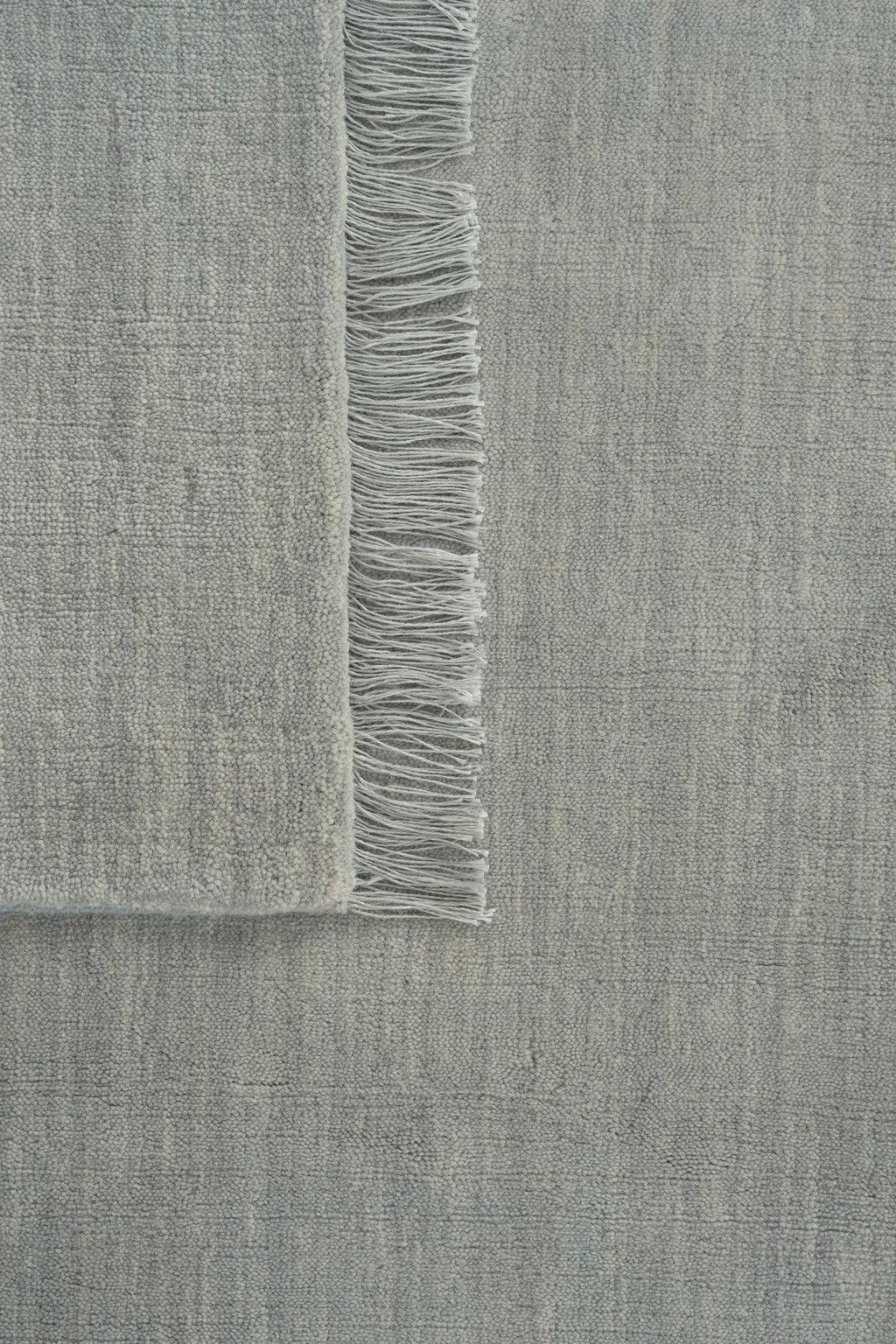 Linie Design Abyss Bliss Wool Rug, a premium hand-knotted wool area rug in soft light grey with a dense, pebbled texture and subtle natural color variations, finished with delicate fringes along one side.