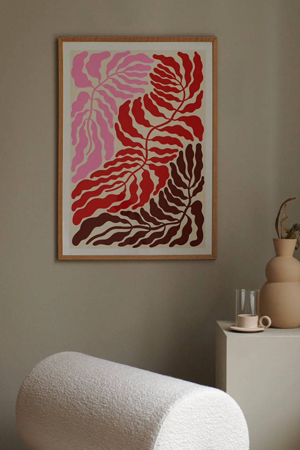 The Poster Club Triple 03, an abstract botanical art print showcasing organic leaf shapes in vibrant blush pink, rich red, and deep burgundy against a cream background, expertly framed in natural oak with a crisp white mat. This contemporary wall art is ideal for creating an organic modern feel in Scandinavian living rooms, bedrooms, or gallery walls.