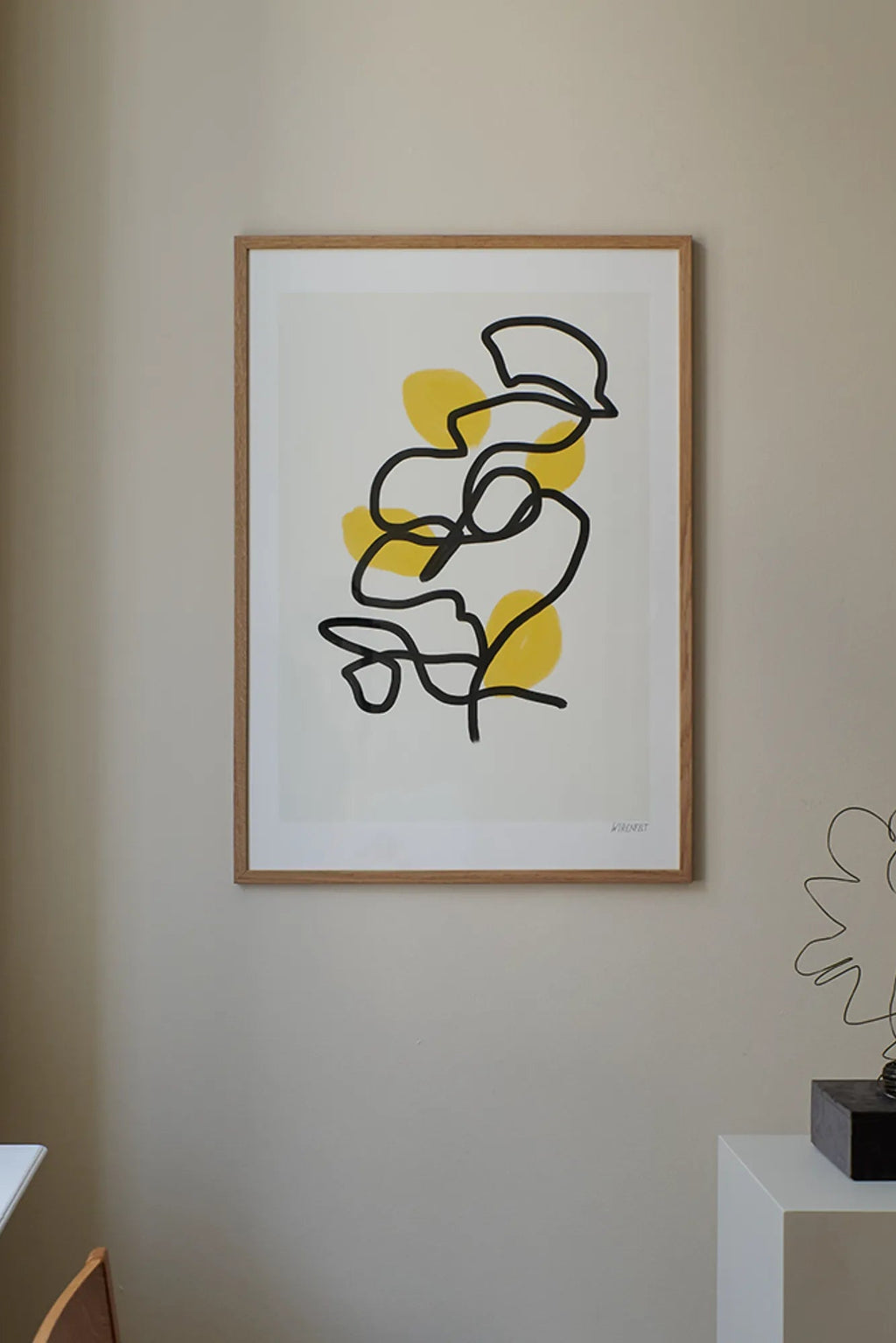 The Poster Club Lemons, an abstract art print featuring bold black continuous line art forming organic shapes, accented with soft yellow abstract forms against a crisp white background, presented in a light natural oak frame.
