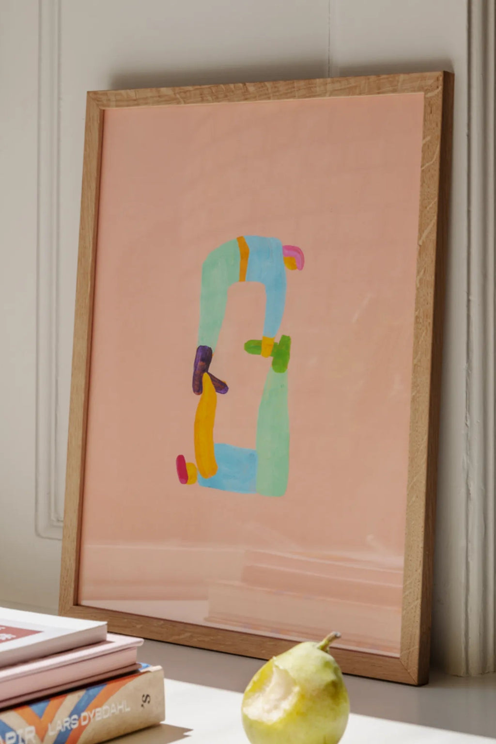 The Poster Club Position 0, a contemporary abstract art print featuring elongated, intertwined figures in soft blue, mint green, yellow, and magenta tones against a gentle blush pink background, framed in light natural oak. This modern minimalist poster offers a playful touch, ideal for gallery wall art, contemporary living rooms, or vibrant nursery decor.