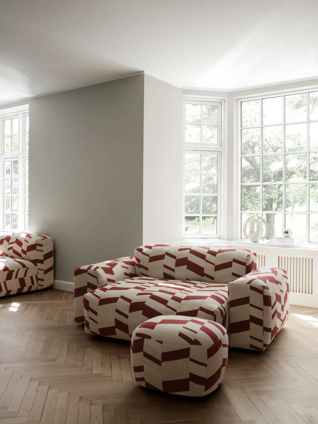 NORR11 Little Big Pouf, a stylish and modern upholstered pouf featuring a geometric pattern of deep red shapes on a natural, textured cream fabric. This elegant pouf adds a playful yet sophisticated accent to contemporary living spaces. Perfect for adding extra seating or a footrest, it appeals to design-conscious homeowners seeking statement pieces.
