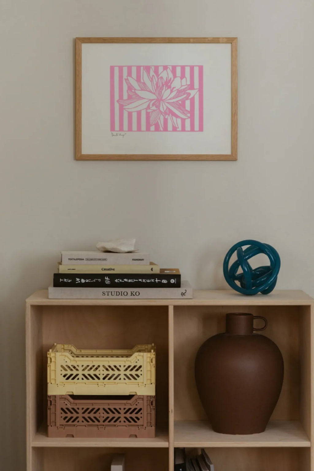 The Poster Club Lotus No 01, a modern graphic art print featuring a detailed white lotus flower illustration against a vibrant pink and white striped background, elegantly framed in a light natural oak wood frame. Perfect as contemporary wall art for minimalist living rooms, Scandinavian bedrooms, or a chic gallery wall accent.
