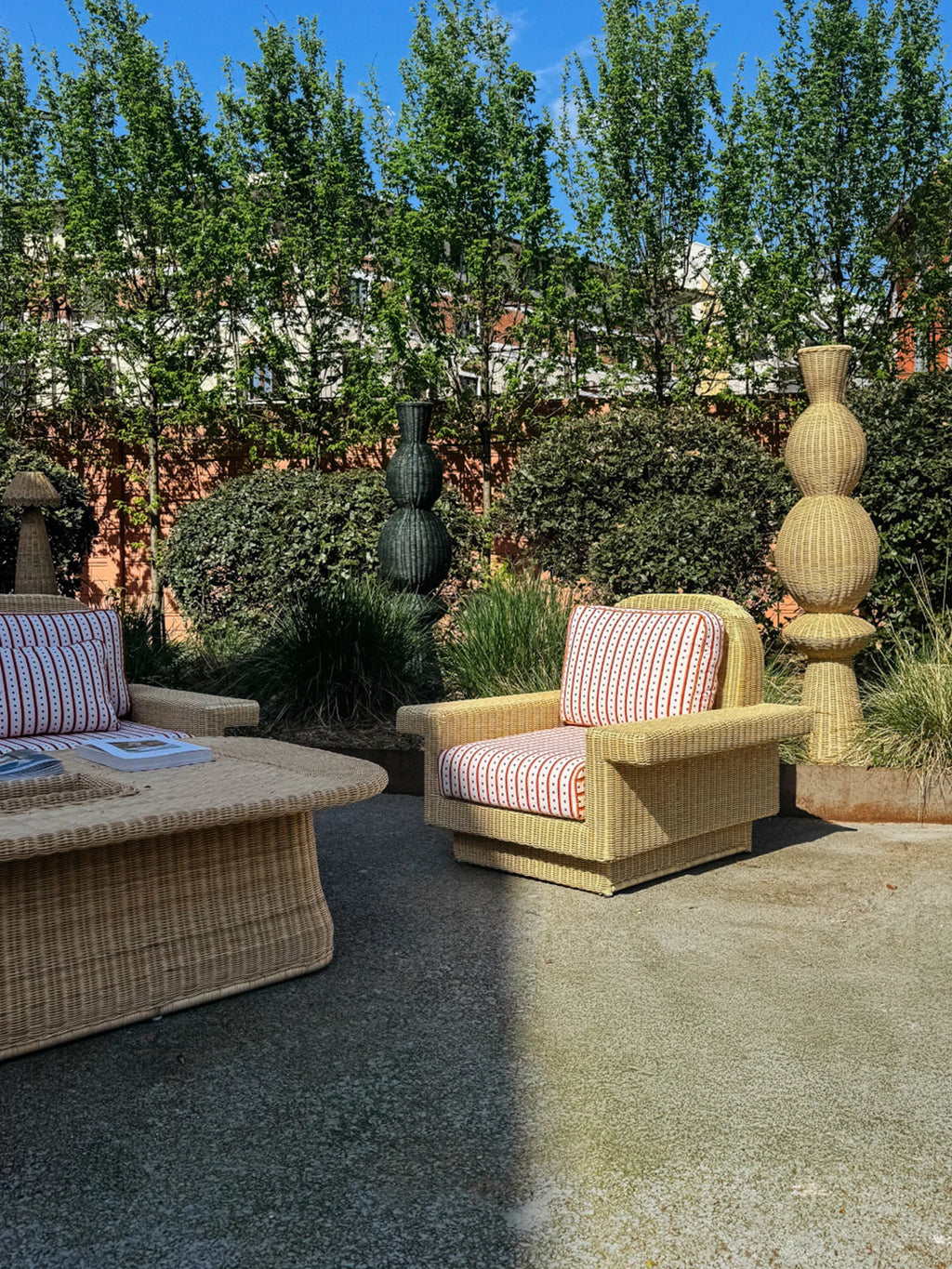 Heaps & Woods Lola Lounge Chair w/ Armrest, a natural light beige woven rattan outdoor lounge chair featuring a structured boxy silhouette with wide armrests and plush cushions upholstered in a vibrant red and white striped fabric. This organic modern rattan patio chair is perfect for creating a stylish coastal living space in your garden, deck, or poolside area.