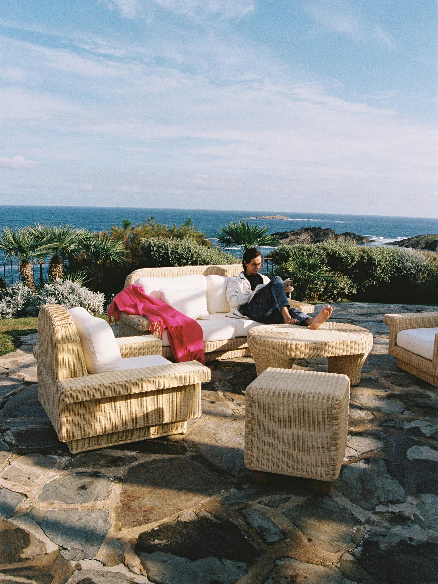 Heaps & Woods Lola Lounge Chair w/ Armrest, a natural hand-woven rattan outdoor lounge chair featuring a light beige woven wicker frame with gently curved armrests and plush cream cushions. This coastal-inspired armchair offers a relaxed, organic modern aesthetic, ideal for creating a luxurious Mediterranean patio or resort-style outdoor living space.